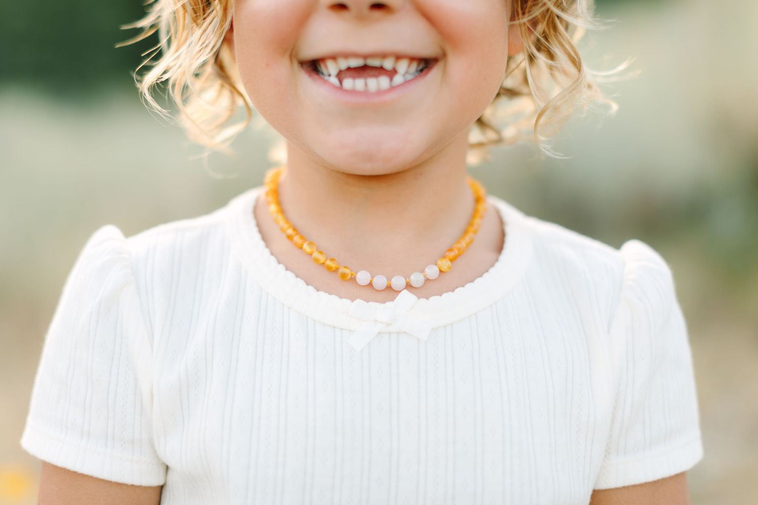 A person in a white dress smiles warmly while standing outdoors in natural lighting.