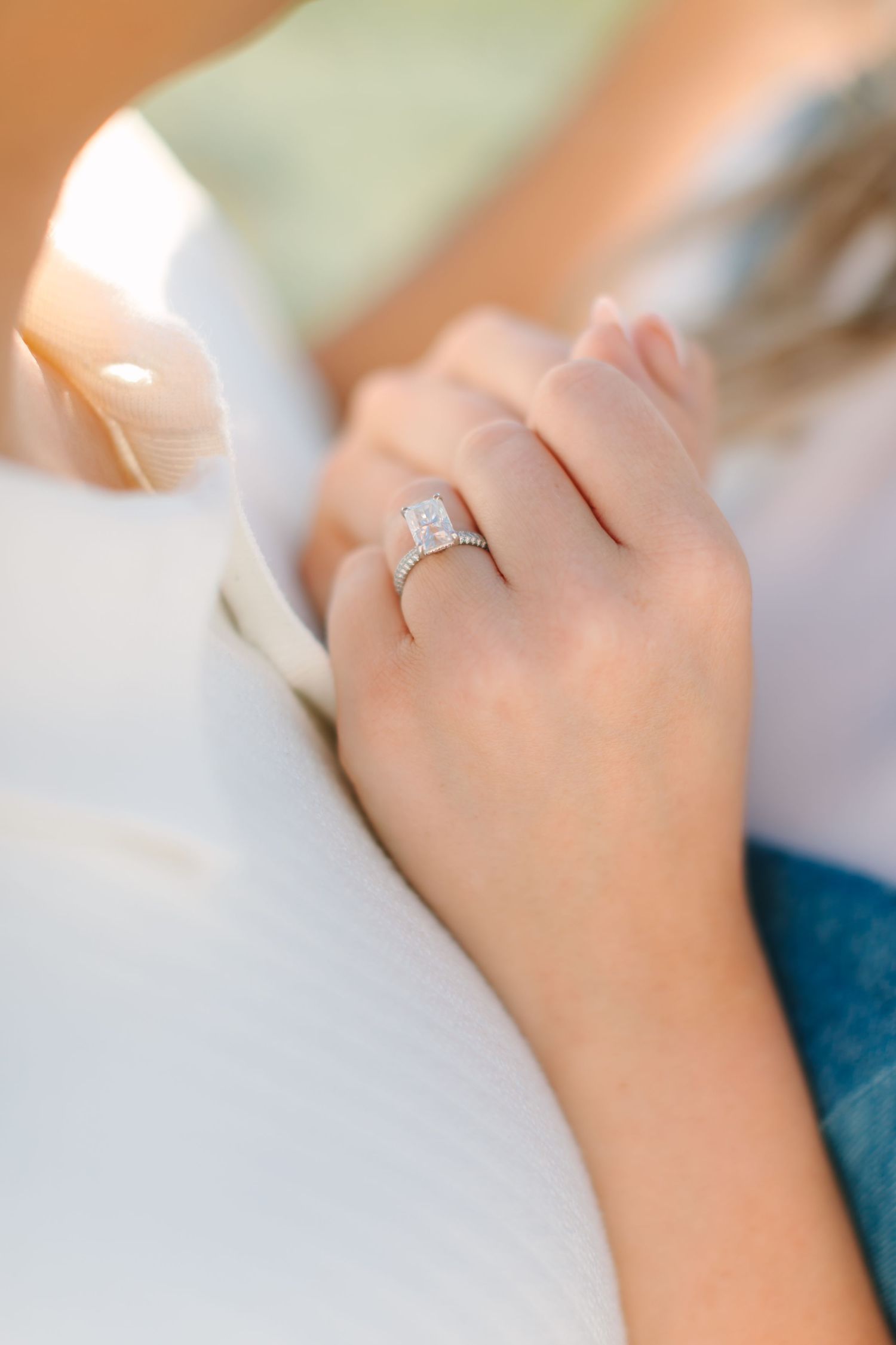 Close-up view of a sparkling diamond engagement ring on a woman's finger against a soft blurred background.