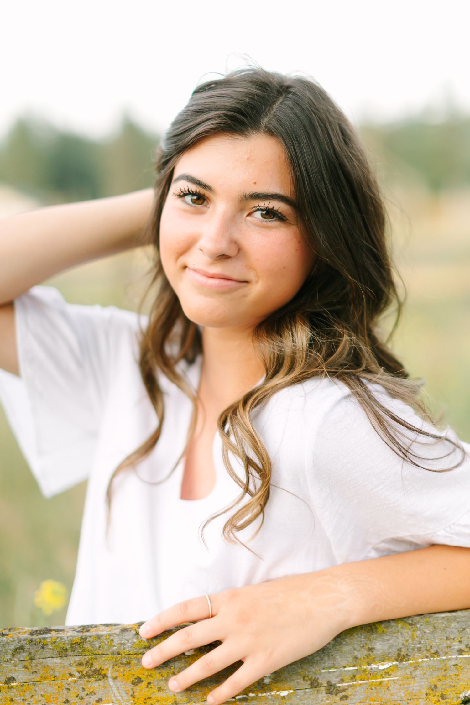 Person in white top poses outdoors against natural background with soft lighting and dreamy expression.