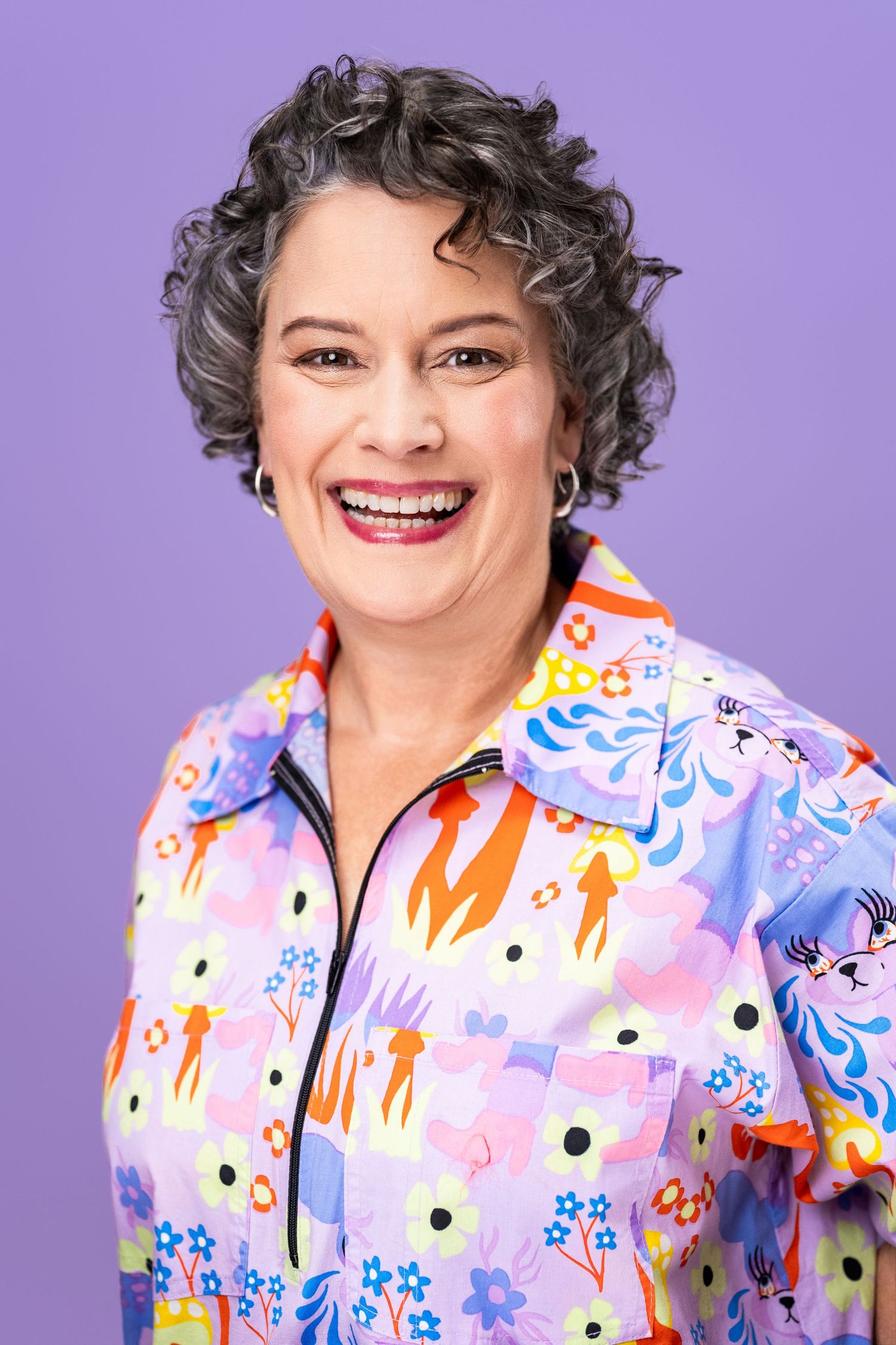 Creative personal branding headshot of a smiling woman with short curly hair against a colorful backdrop