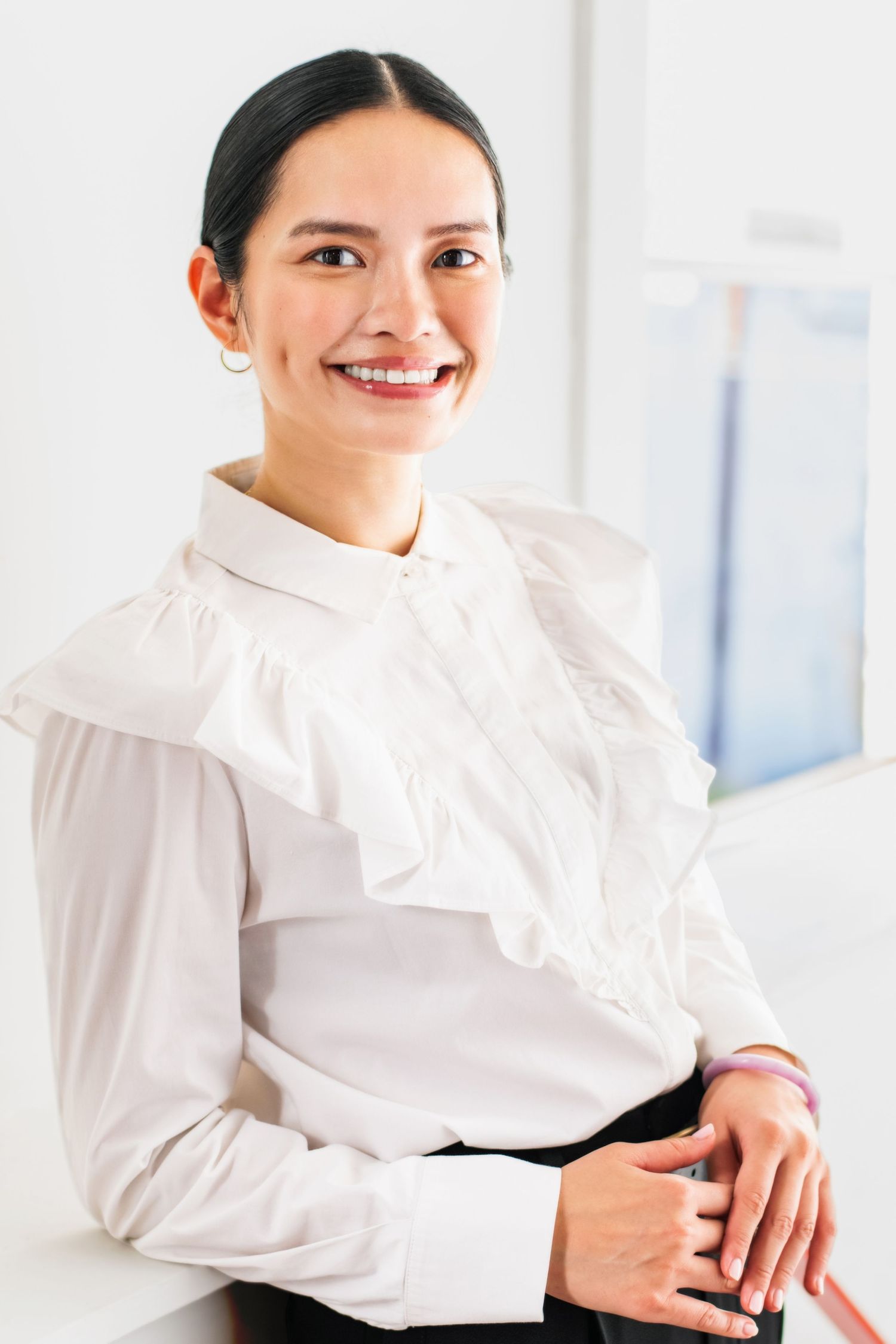 Clean corporate headshot of a female professional in a white blouse, photographed in a bright office environment with an approachable look.