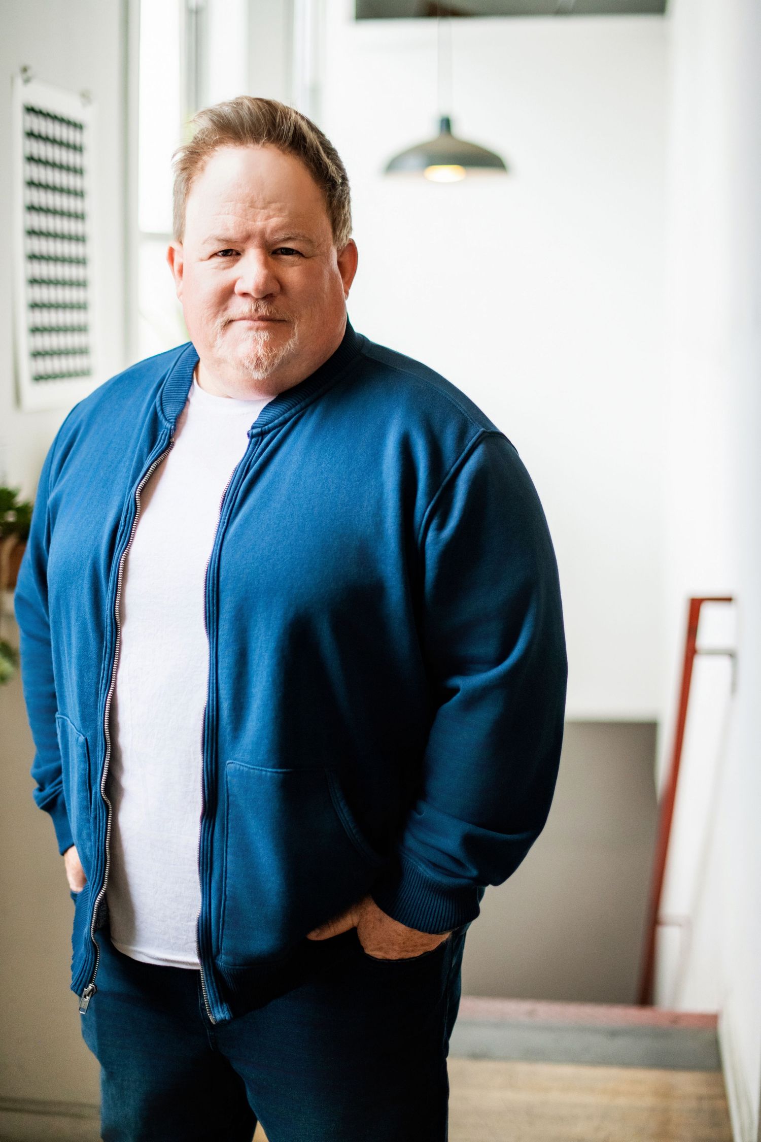 Lifestyle headshot of a man in a blue jacket, photographed indoors with soft natural light for an approachable, authentic portrait.