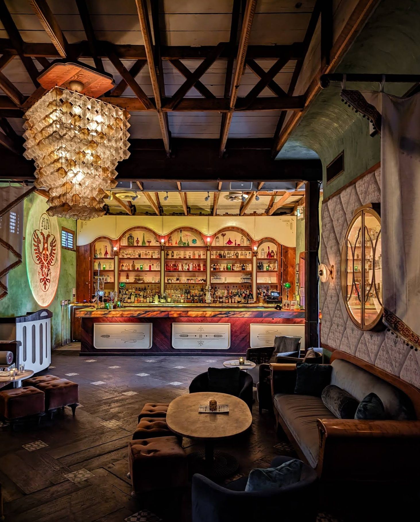 Interior of Apotheke cocktail bar with ornate chandelier, velvet seating, and a warmly lit bar lined with bottles.