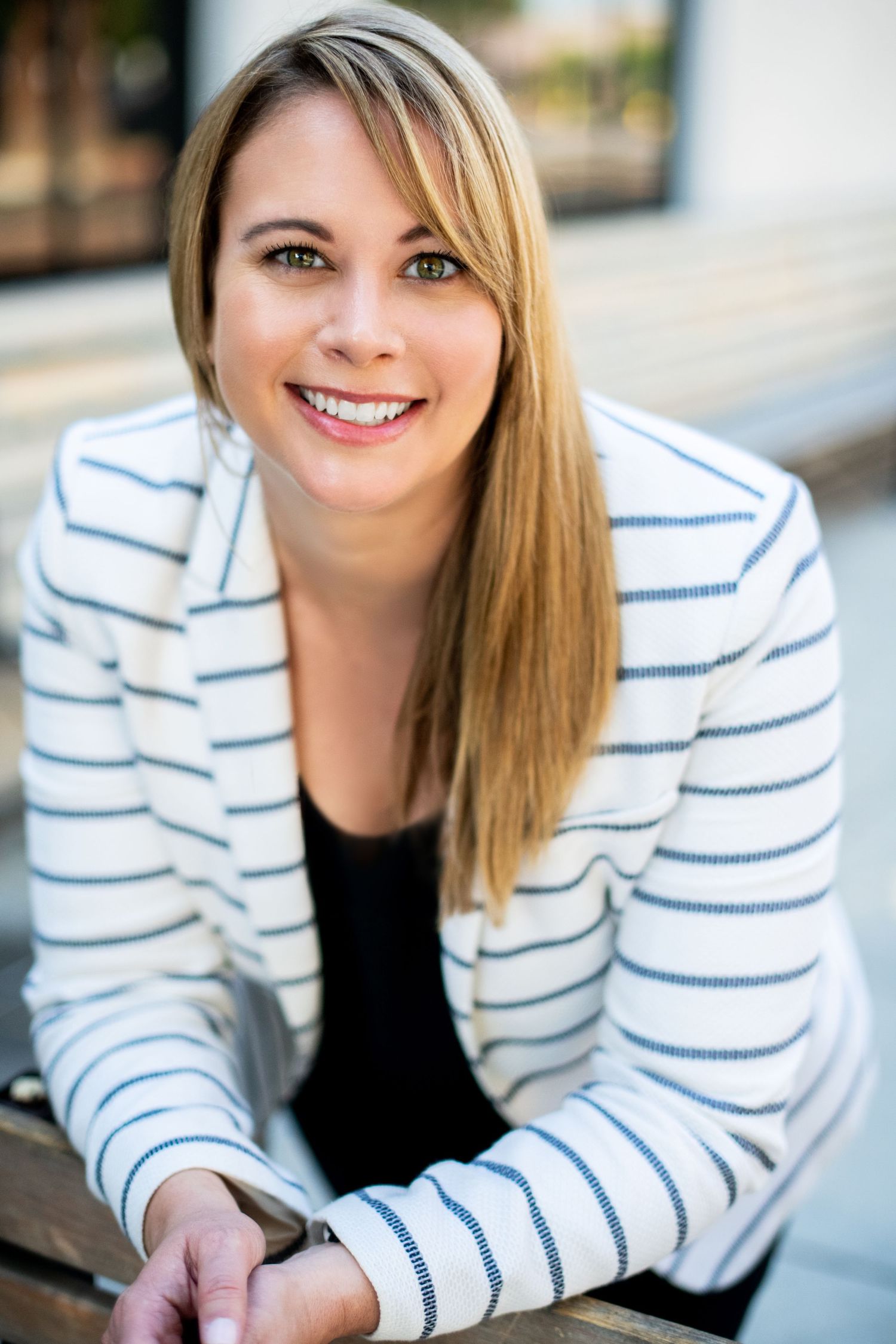 Professional female business headshot of a woman in a white striped blazer, smiling naturally in an outdoor setting in Los Angeles.