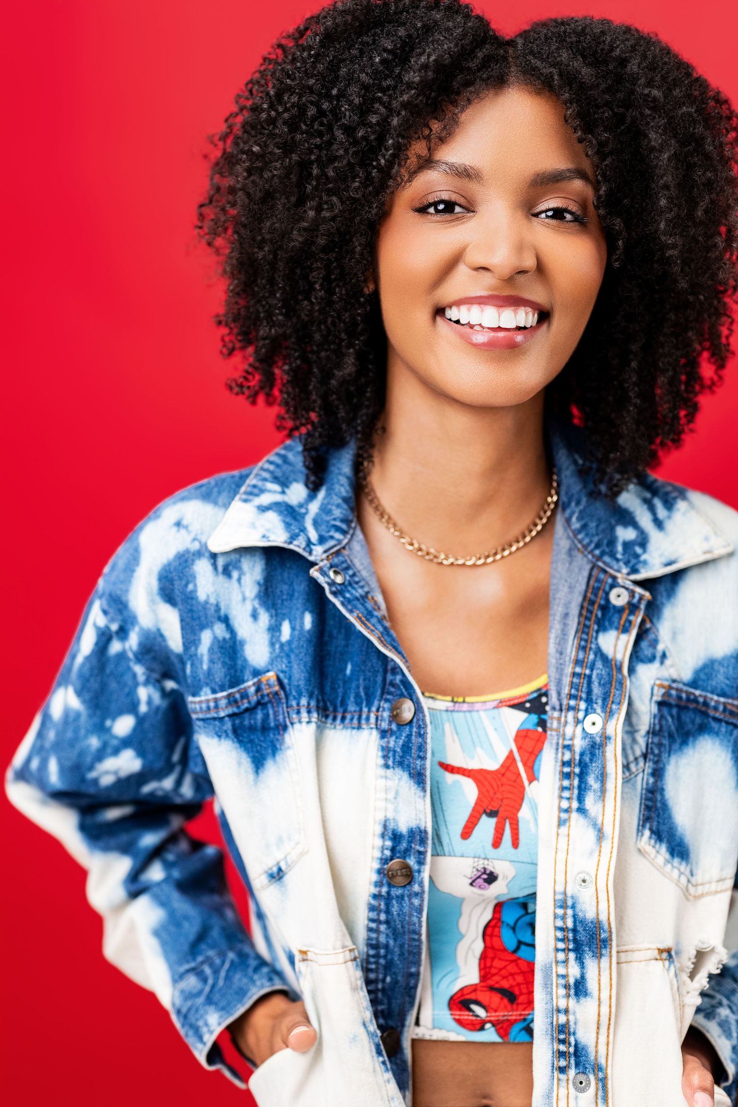 Bright, expressive actor headshot of a smiling woman in colorful wardrobe against a red backdrop at Nice Headshots in Los Angeles.