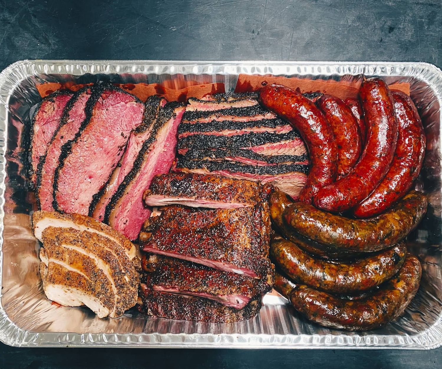 Assorted smoked meats in a silver catering tray at Moo’s Craft Barbecue.