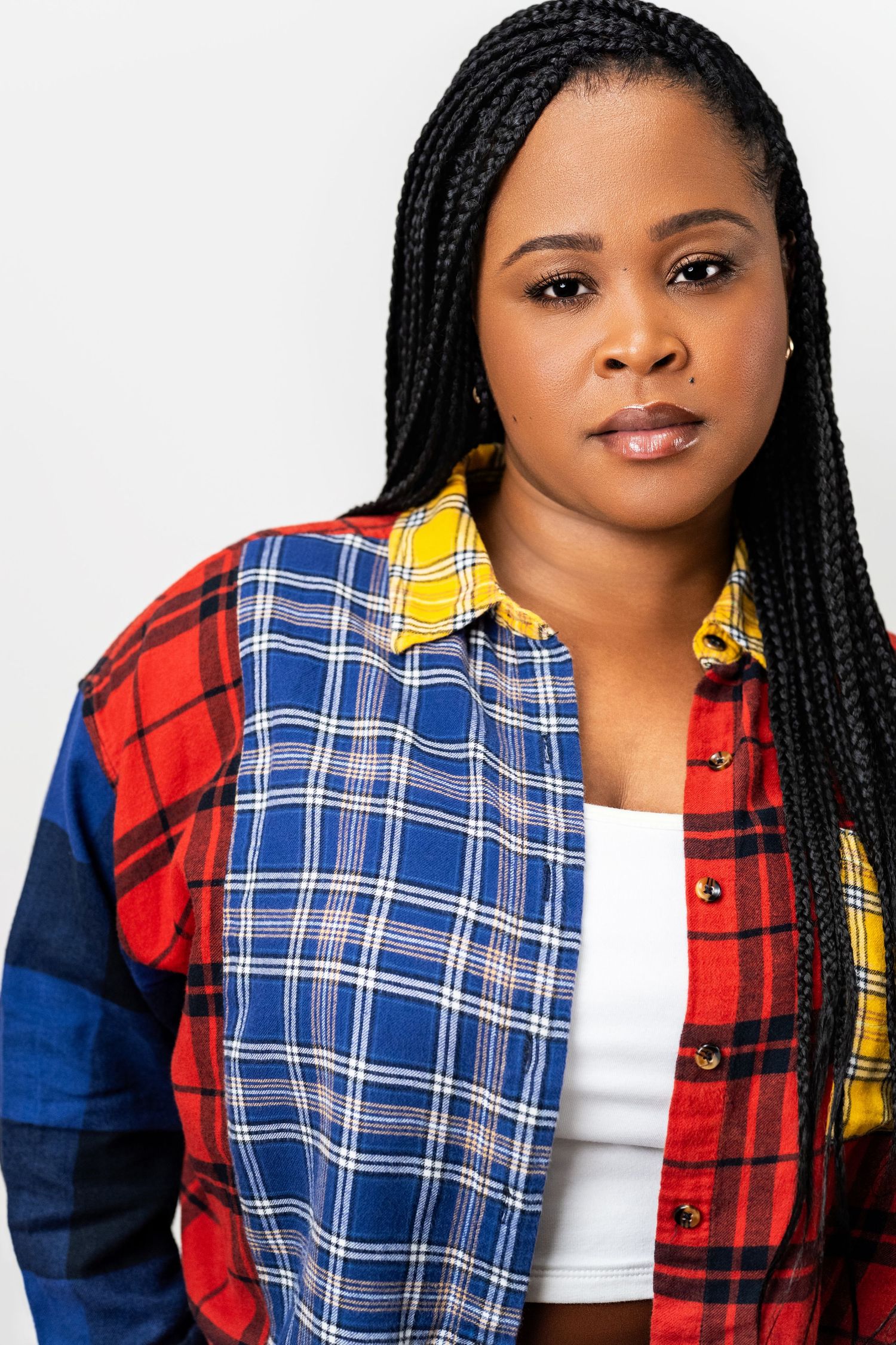 Theatrical actor headshot of a confident woman with braids in a plaid shirt on a clean neutral background in Los Angeles.