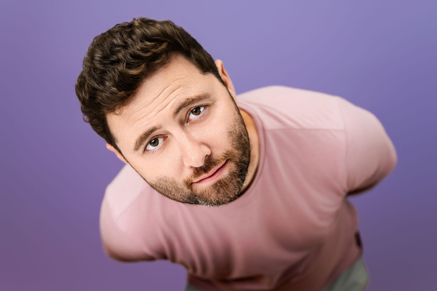 David Kearney, employee of Nice Headshots, photographed in the studio with a relaxed expression against a purple background.
