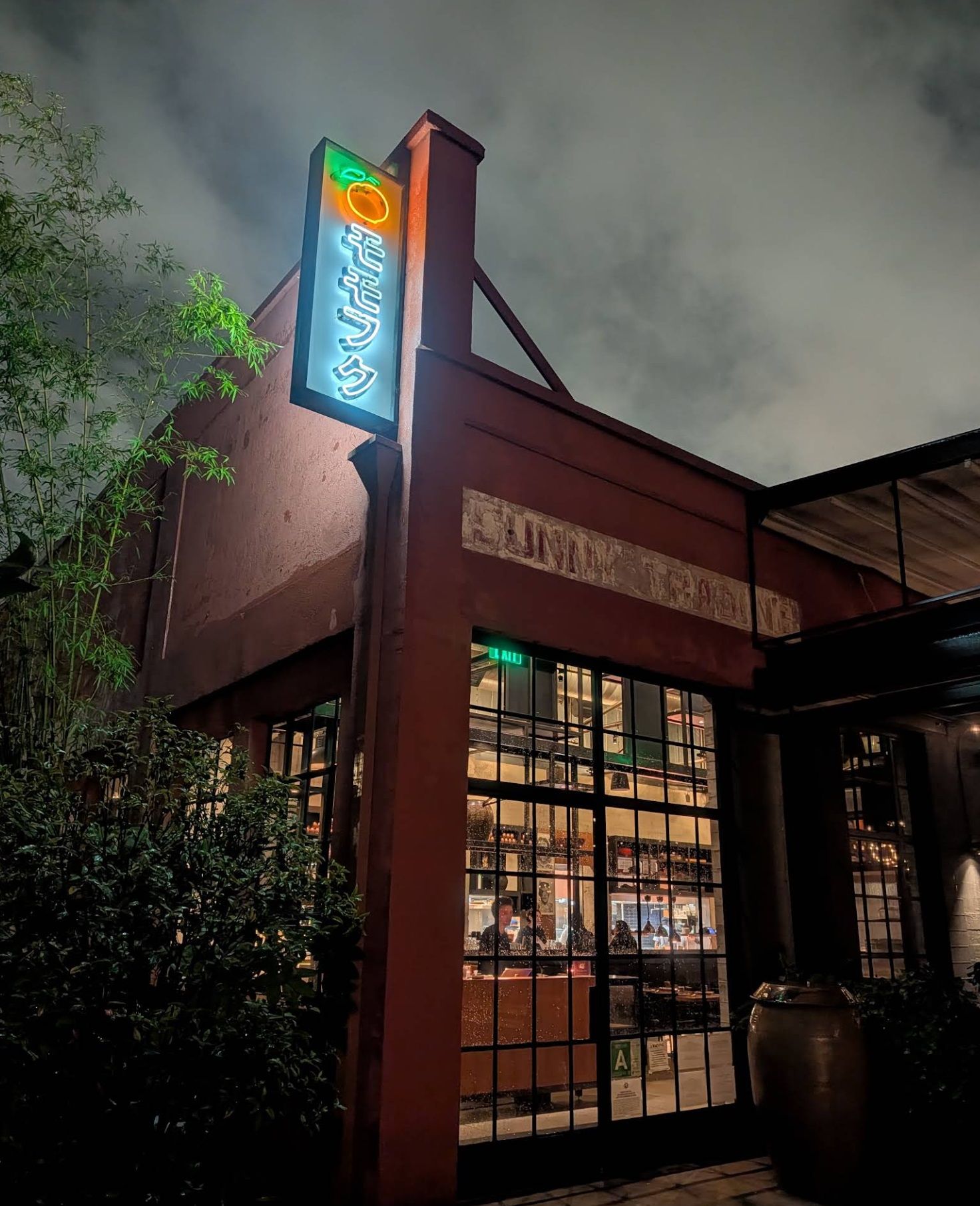 Exterior of Majordomo in Downtown Los Angeles at night with interior lights glowing and neon signage illuminated.