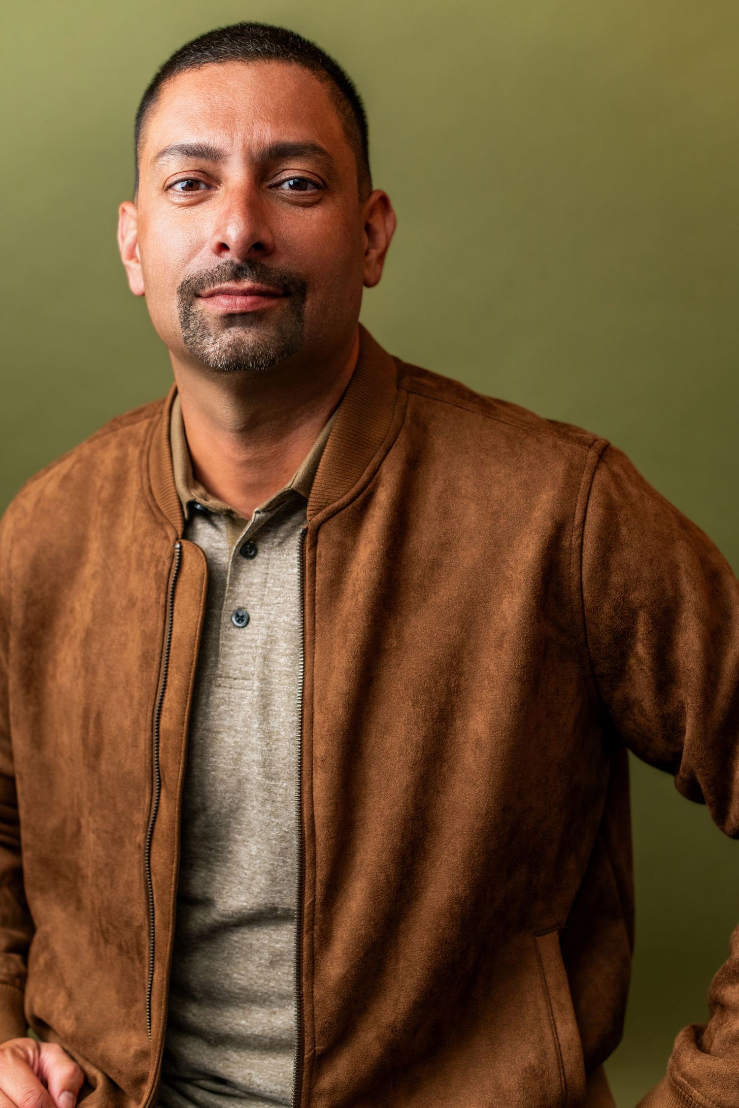 Male business professional wearing a brown jacket, photographed against an olive green backdrop for a professional headshot in Los Angeles.