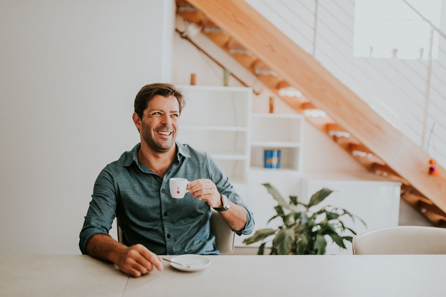 Lifestyle headshot of a man holding an espresso cup, smiling naturally in a bright modern interior for a relaxed professional portrait.