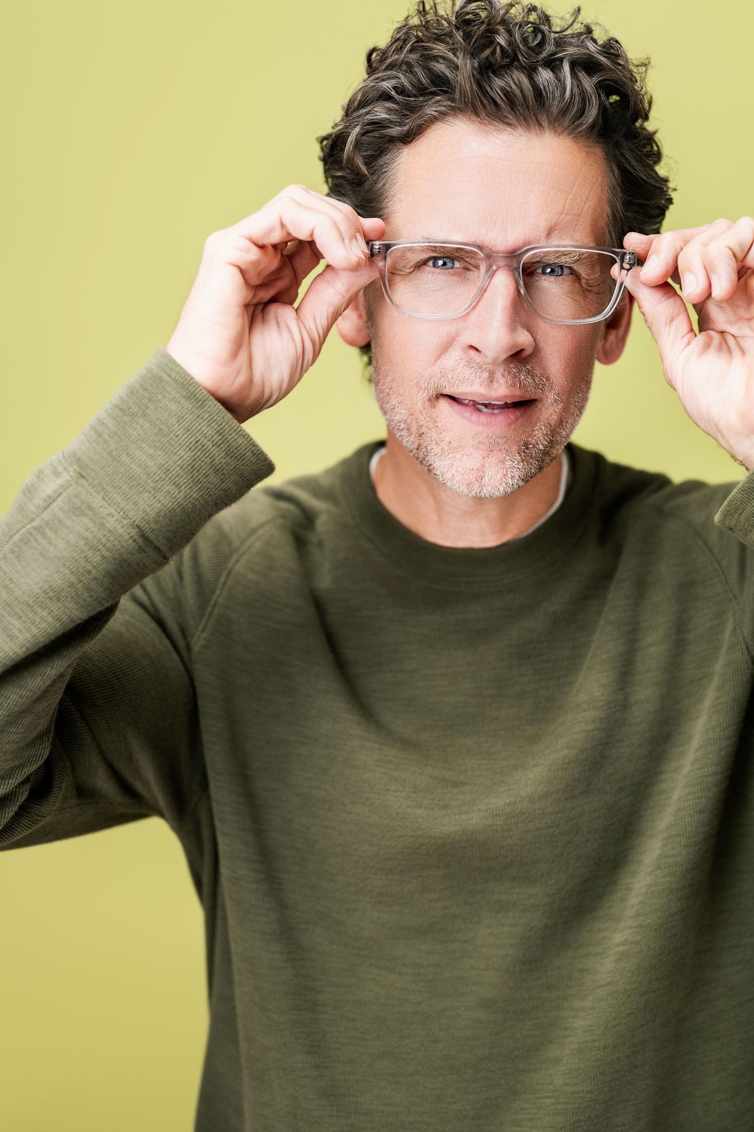 Expressive professional headshot of a man adjusting his glasses against a green studio backdrop at Nice Headshots in Los Angeles.