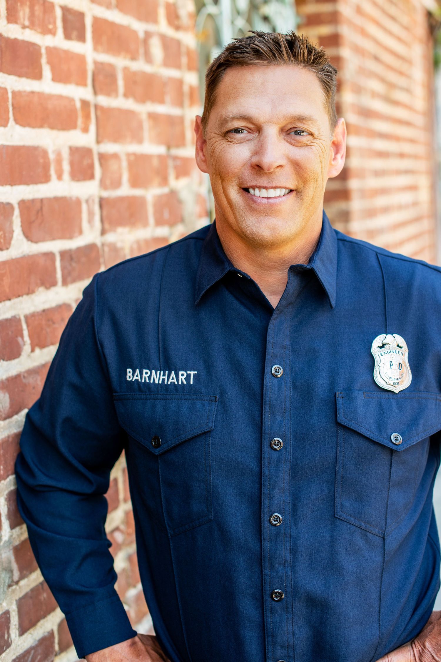 Professional Fireman wearing a navy work shirt, photographed against a brick wall for a professional business headshot in Los Angeles.