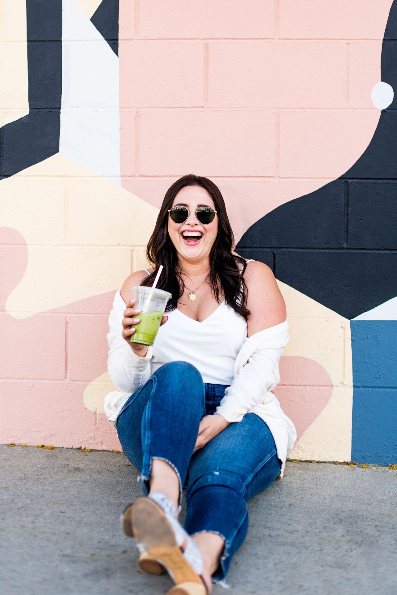 Personal branding photography in Los Angeles of a smiling woman with a drink against a colorful mural