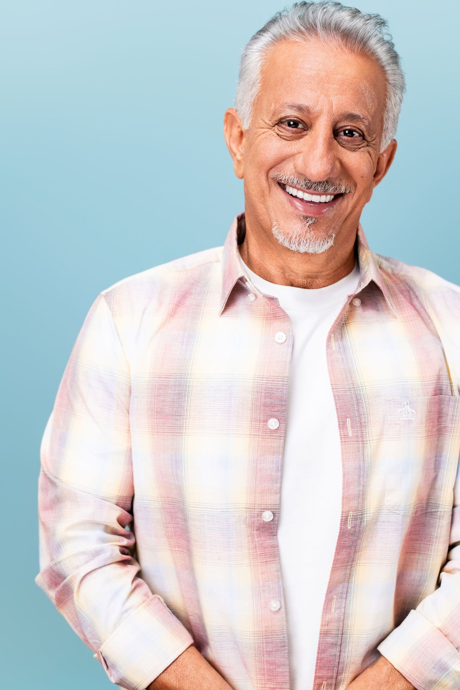 Smiling older man with gray hair wearing a pastel plaid shirt on a light blue background, photographed in a Los Angeles headshot studio
