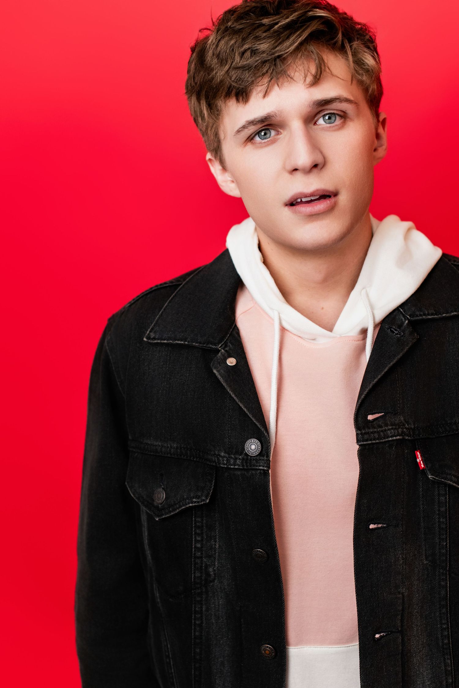 Young adult actor headshot featuring an expressive male on a bold red background, suited for commercial casting in Los Angeles.