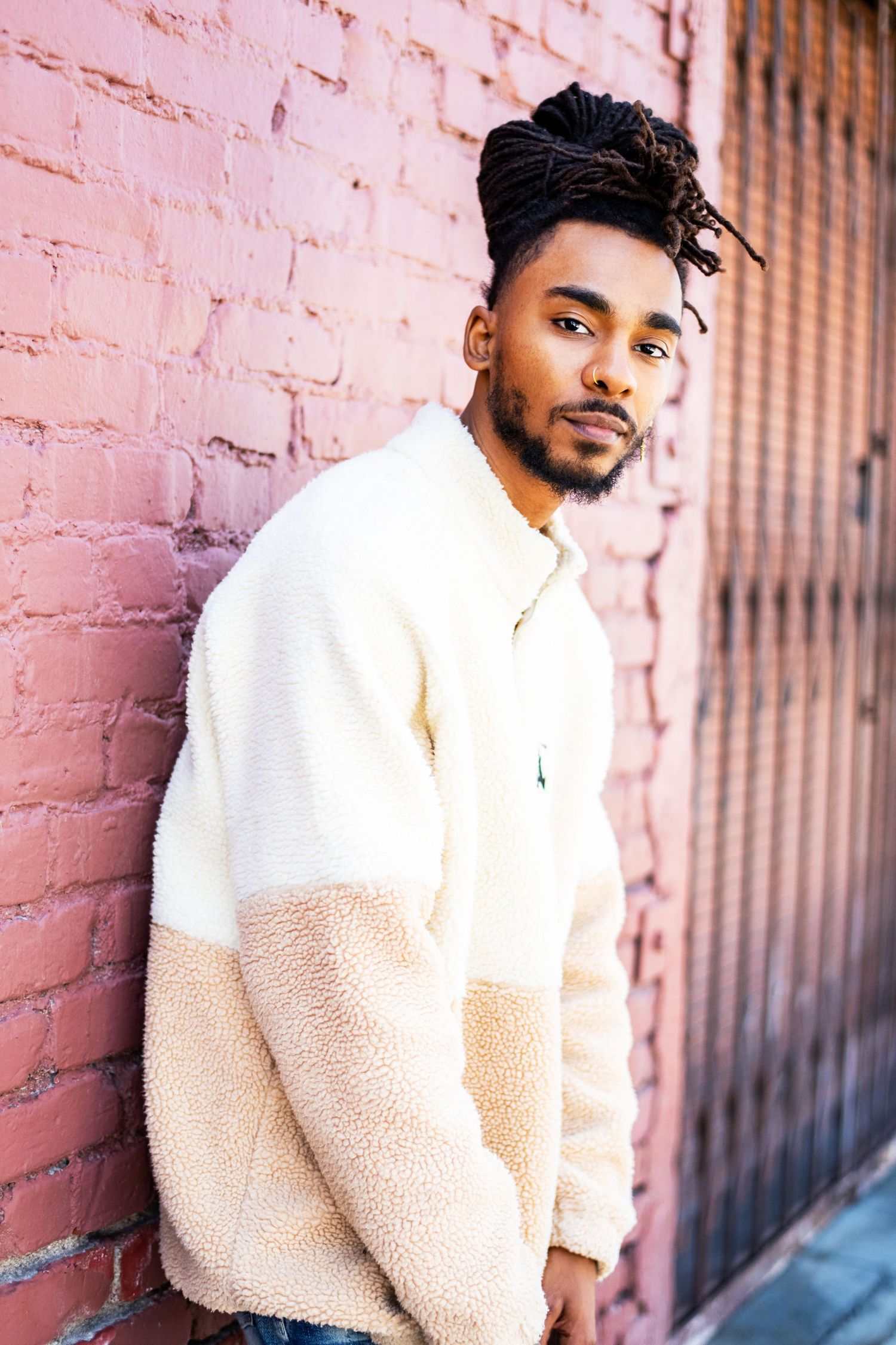 Male model leaning against a brick wall wearing a fleece jacket, photographed outdoors for a lifestyle modeling headshot in Los Angeles.