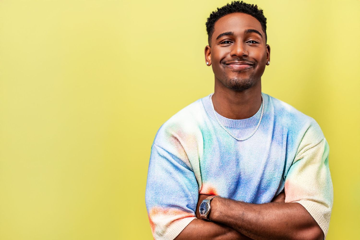 Confident man with arms crossed photographed at a Los Angeles headshot studio against a yellow background.