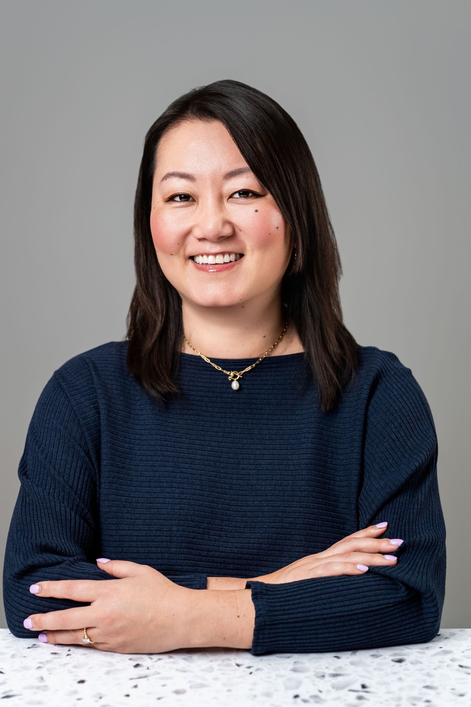 Professional business headshot of a woman in a navy top against a clean gray studio background in Los Angeles.