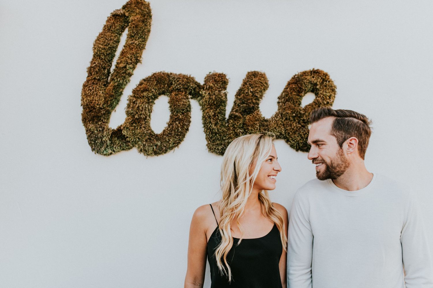 Engaged couple smiles at each other under a 'Love' sign, capturing the essence of storytelling in wedding and engagement photography.