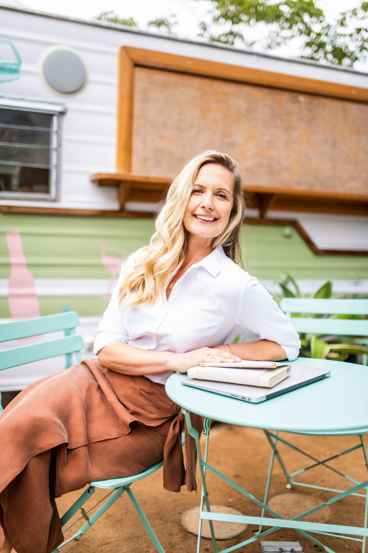 Lifestyle headshot of professional woman seated at outdoor café table in Los Angeles with laptop and notebook, natural light portrait.