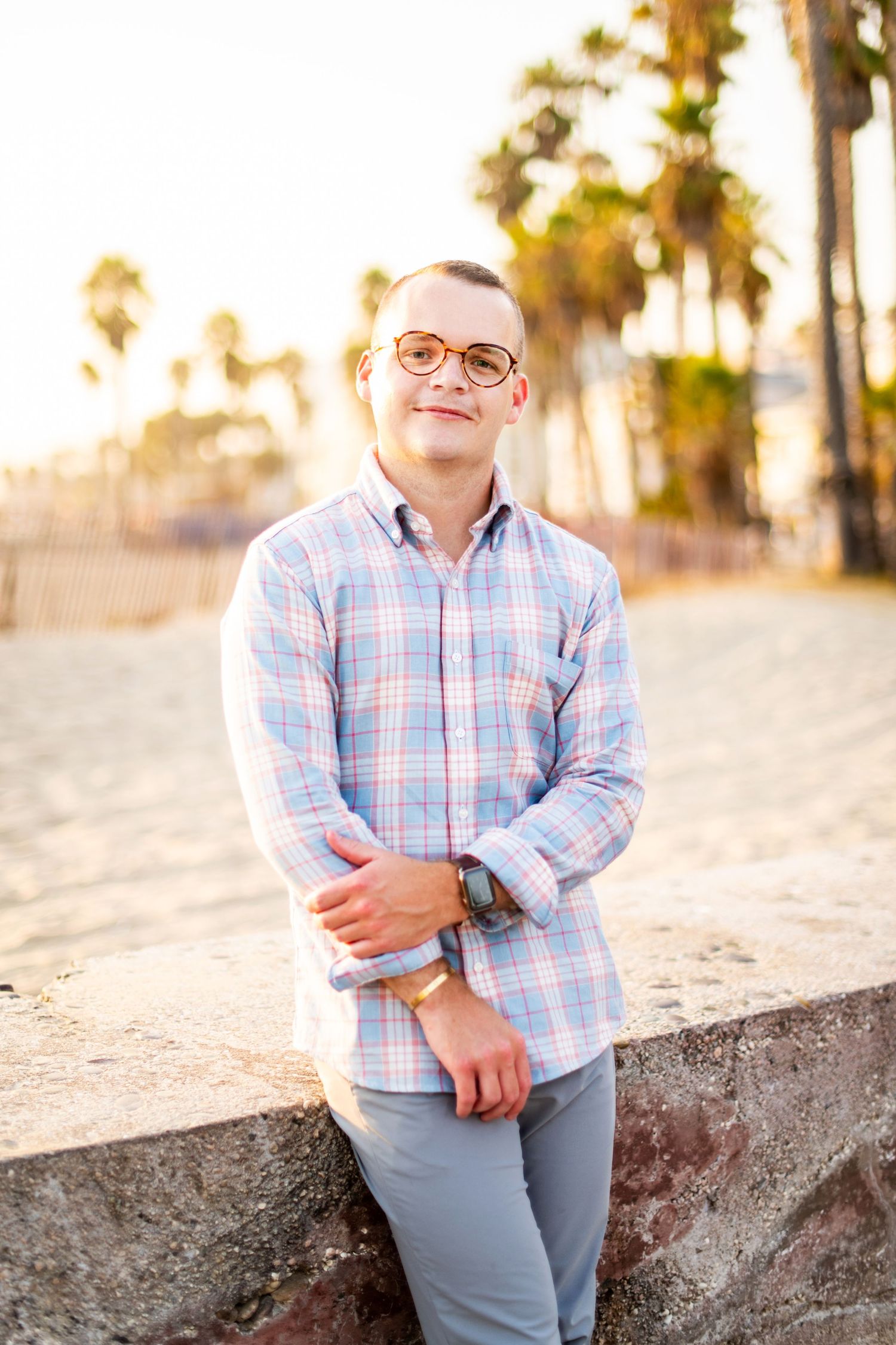 Lifestyle headshot of a man standing near the beach with palm trees in the background, captured in warm natural light.