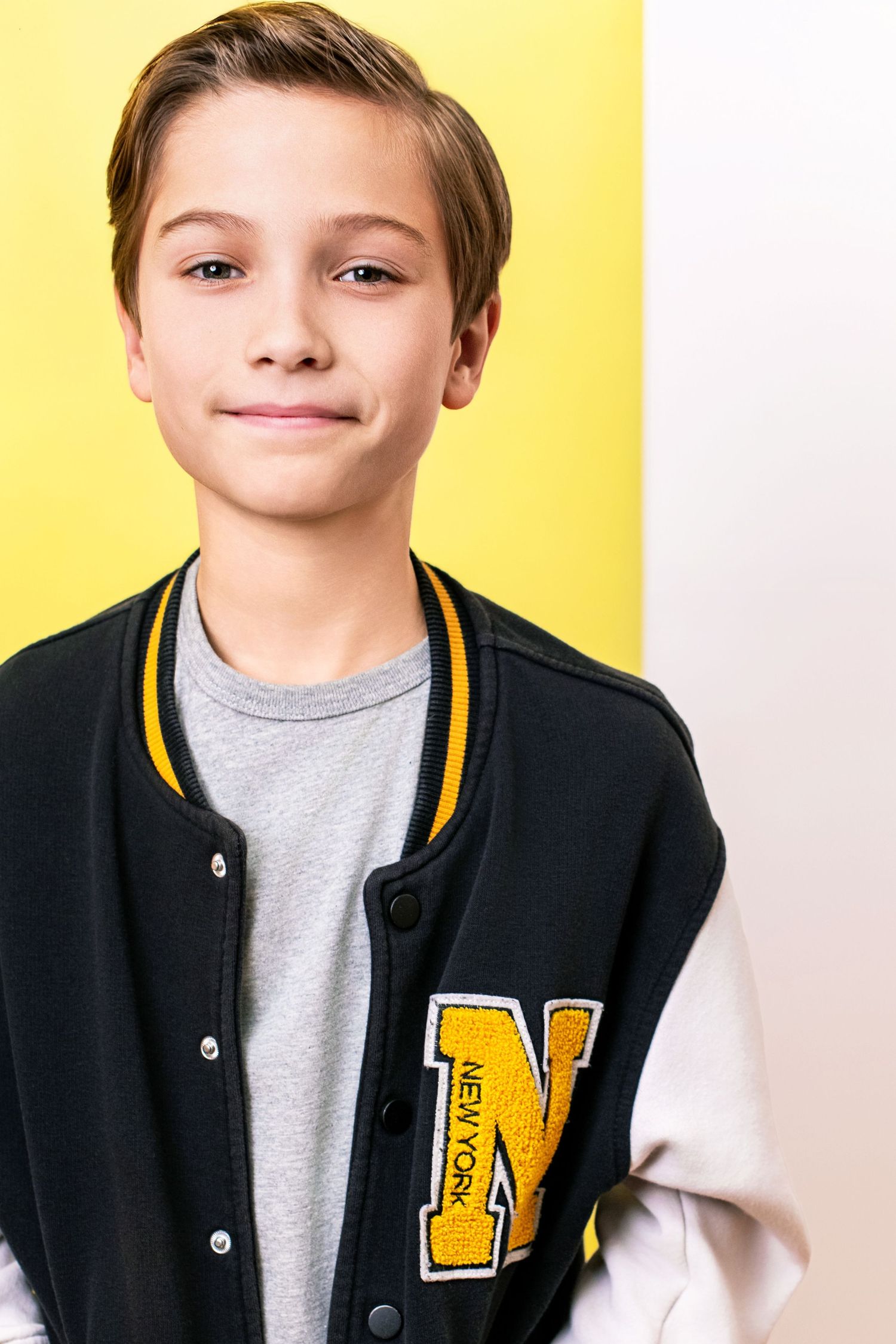 Child actor headshot with a confident, friendly expression against a yellow backdrop, photographed in Los Angeles for youth casting