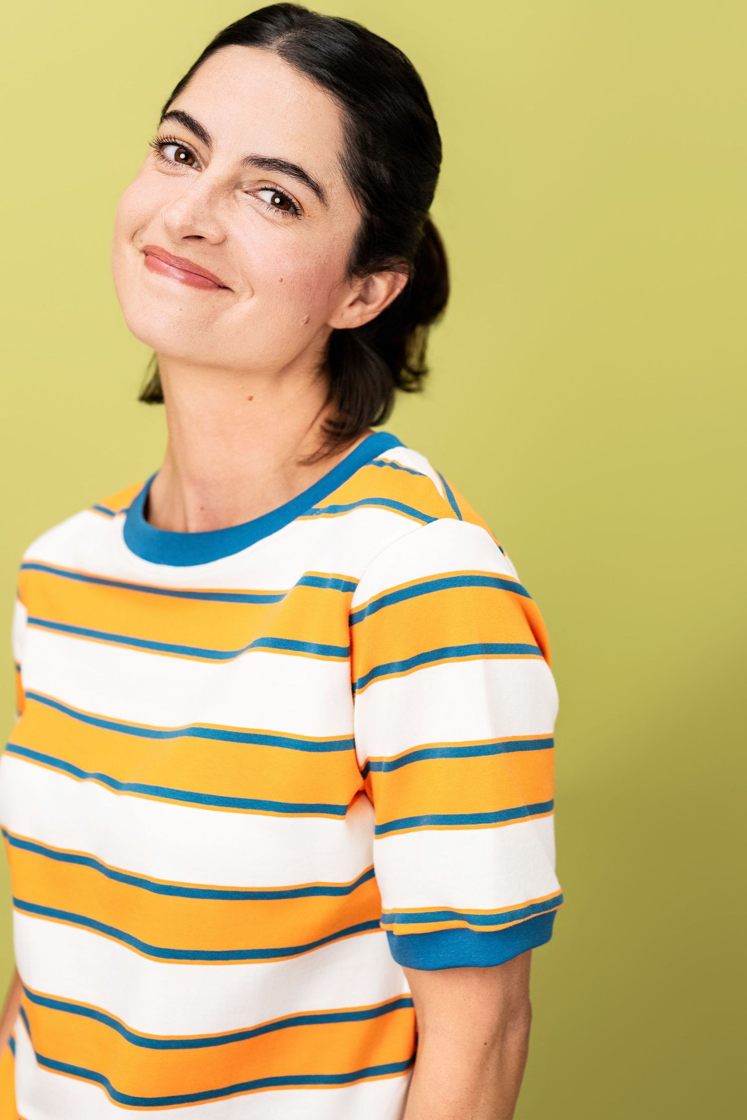 Commercial actor headshot of a smiling woman in a striped top against a soft green backdrop in Los Angeles.
