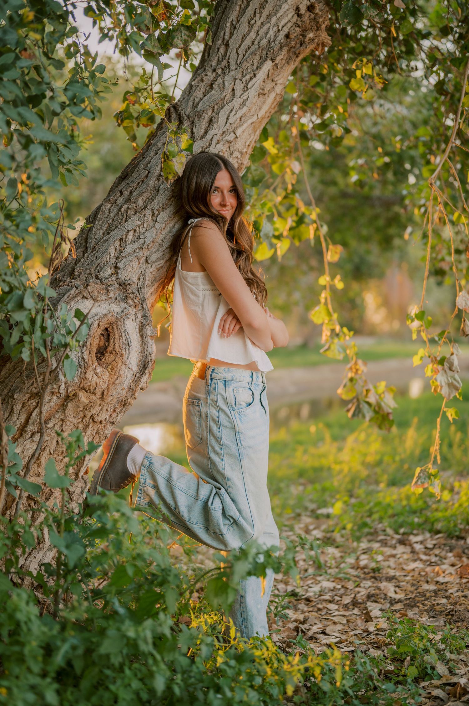 Senior leaning against tree with soft light filtering through leaves by canal