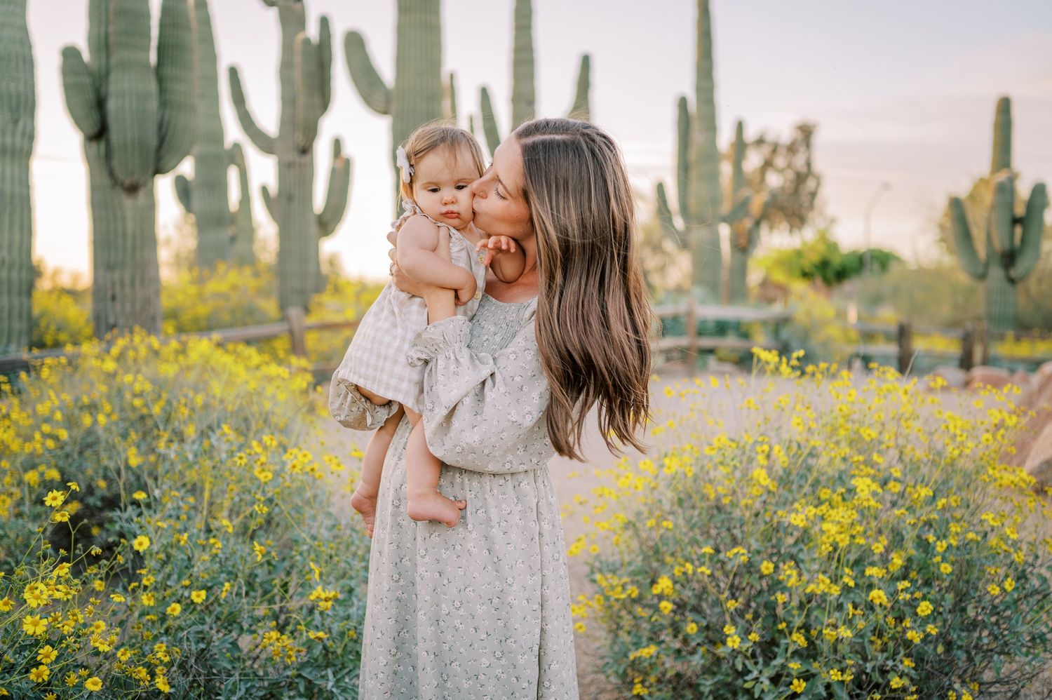 A tender moment shared in a desert landscape with blooming yellow wildflowers and towering saguaro cacti in the background.