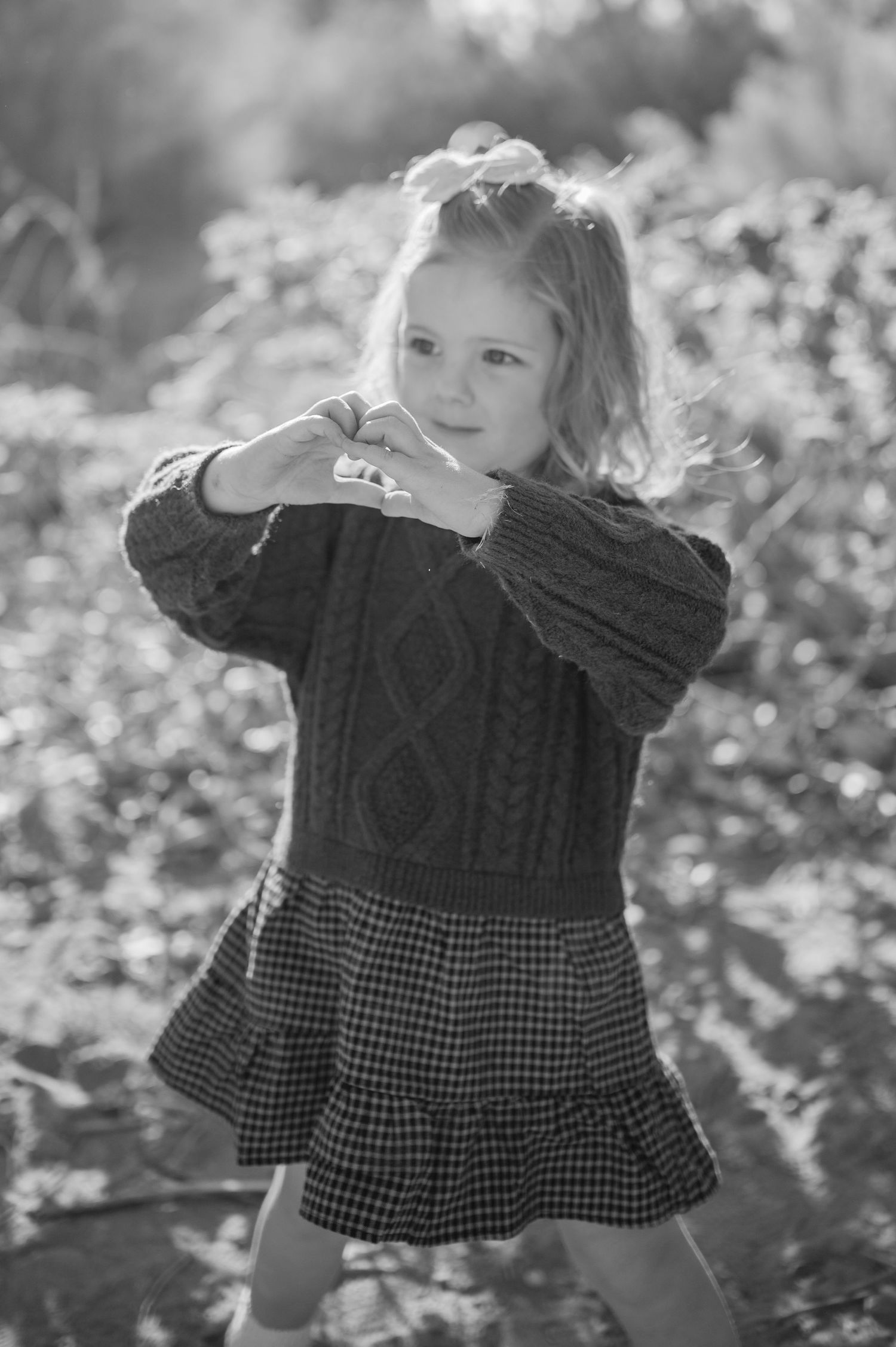 A young child in a black and white checkered dress poses playfully in a series of black and white outdoor photos.