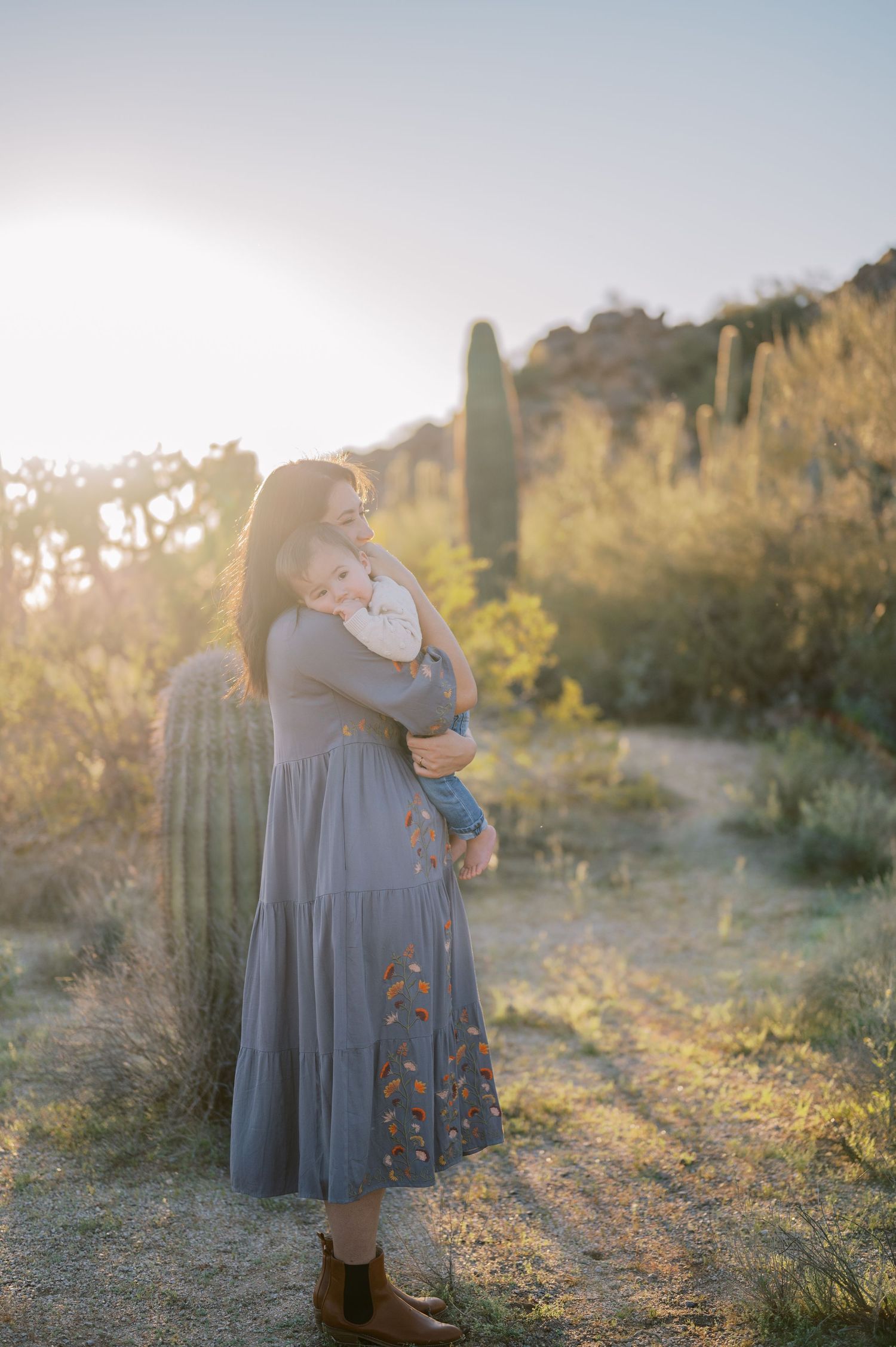 A tender embrace between two figures in a desert landscape at golden hour with warm sunlight filtering through.