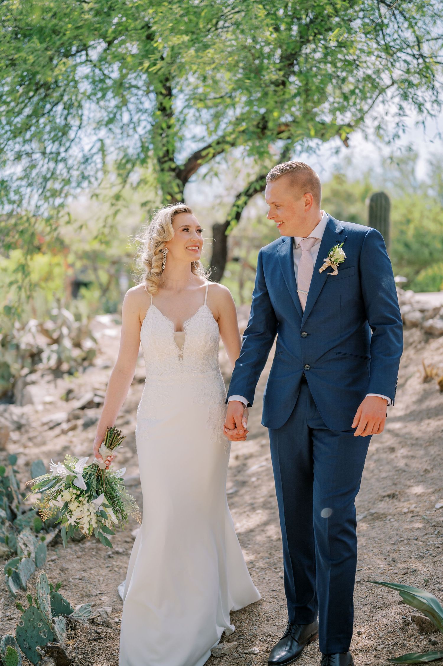 A couple in wedding attire walks hand in hand along a desert path. Phoenix Arizona couples photographer.