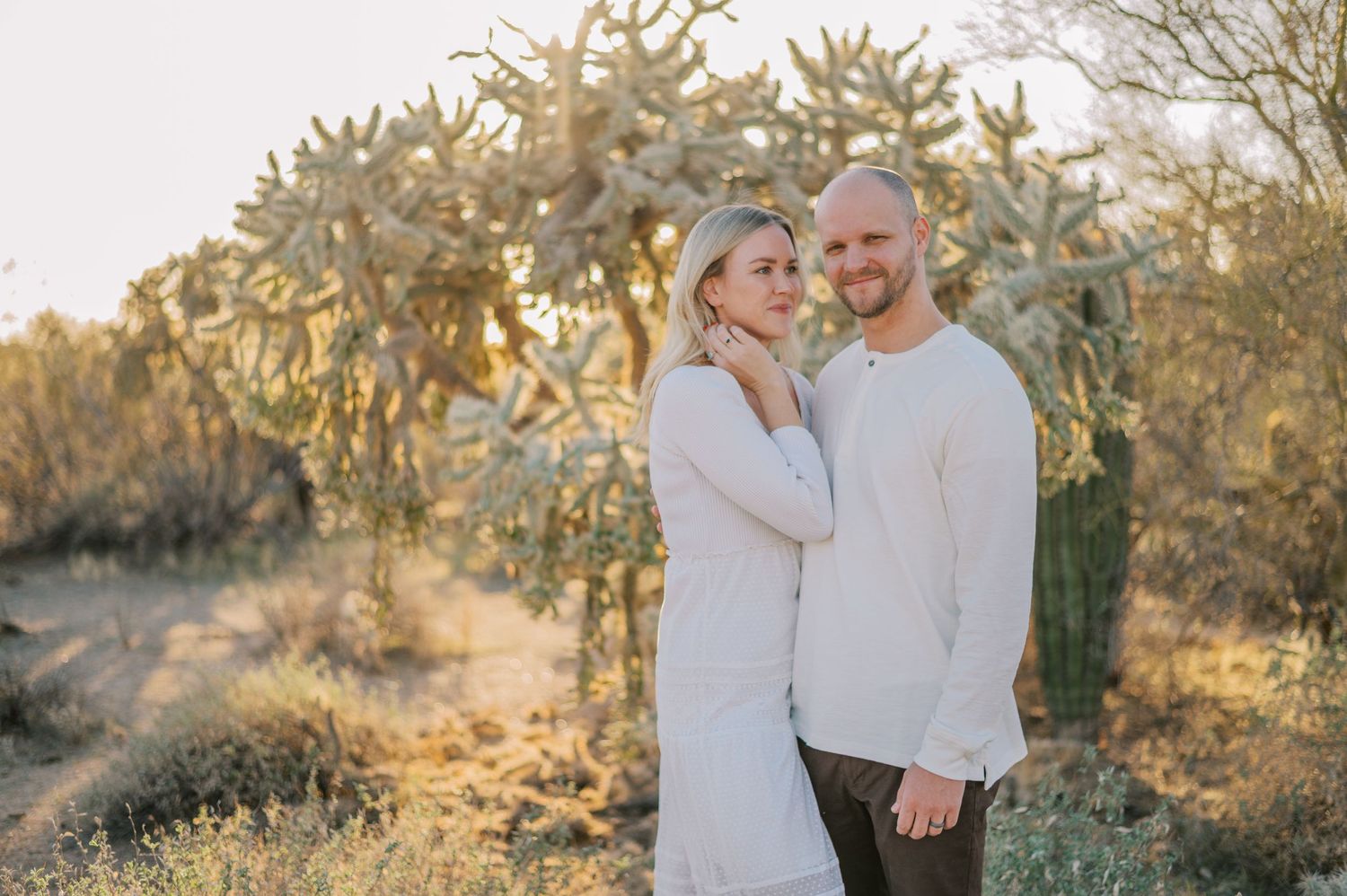 A couple embraces during a golden hour photoshoot in a desert landscape with saguaro cacti. Phoenix Arizona couples photographer.