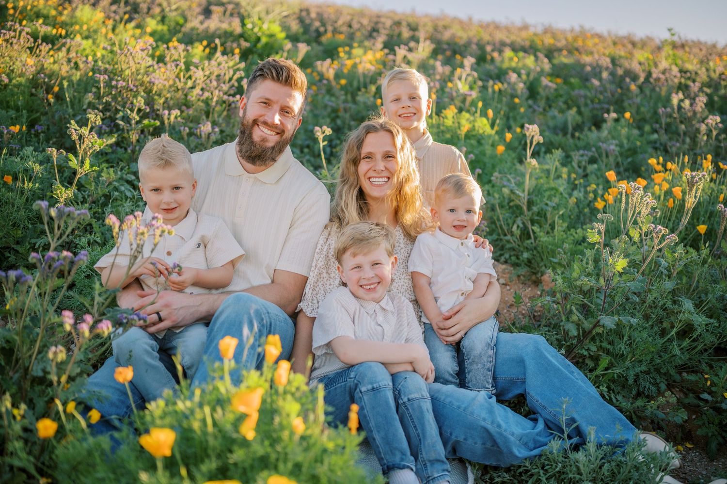 A group sits together on a hillside surrounded by vibrant yellow wildflowers during golden hour. Phoenix Arizona family photographer.
