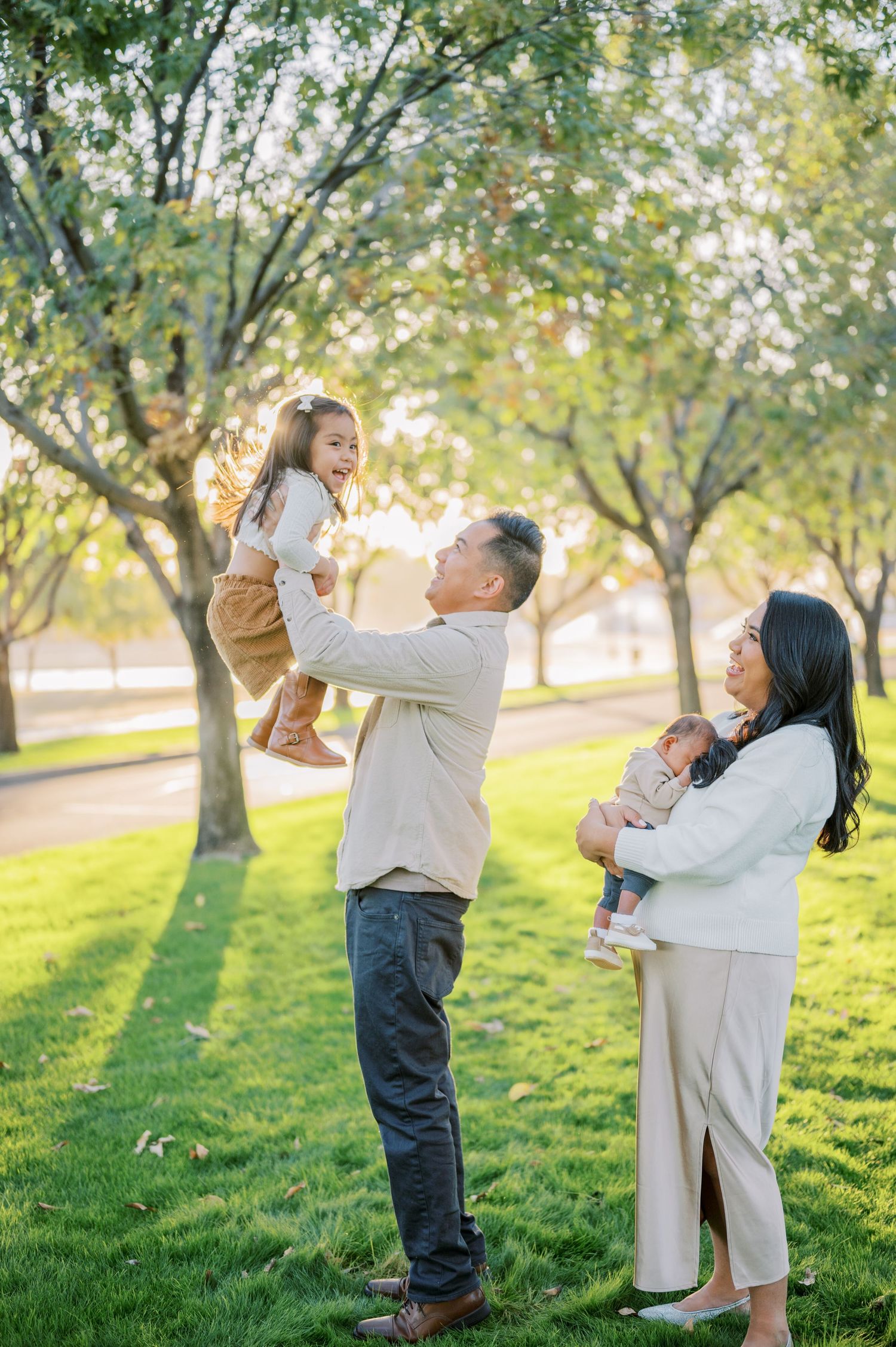 Candid outdoor family moments captured in a grassy park setting with sunlit trees in the background. Phoenix Arizona family photographer.