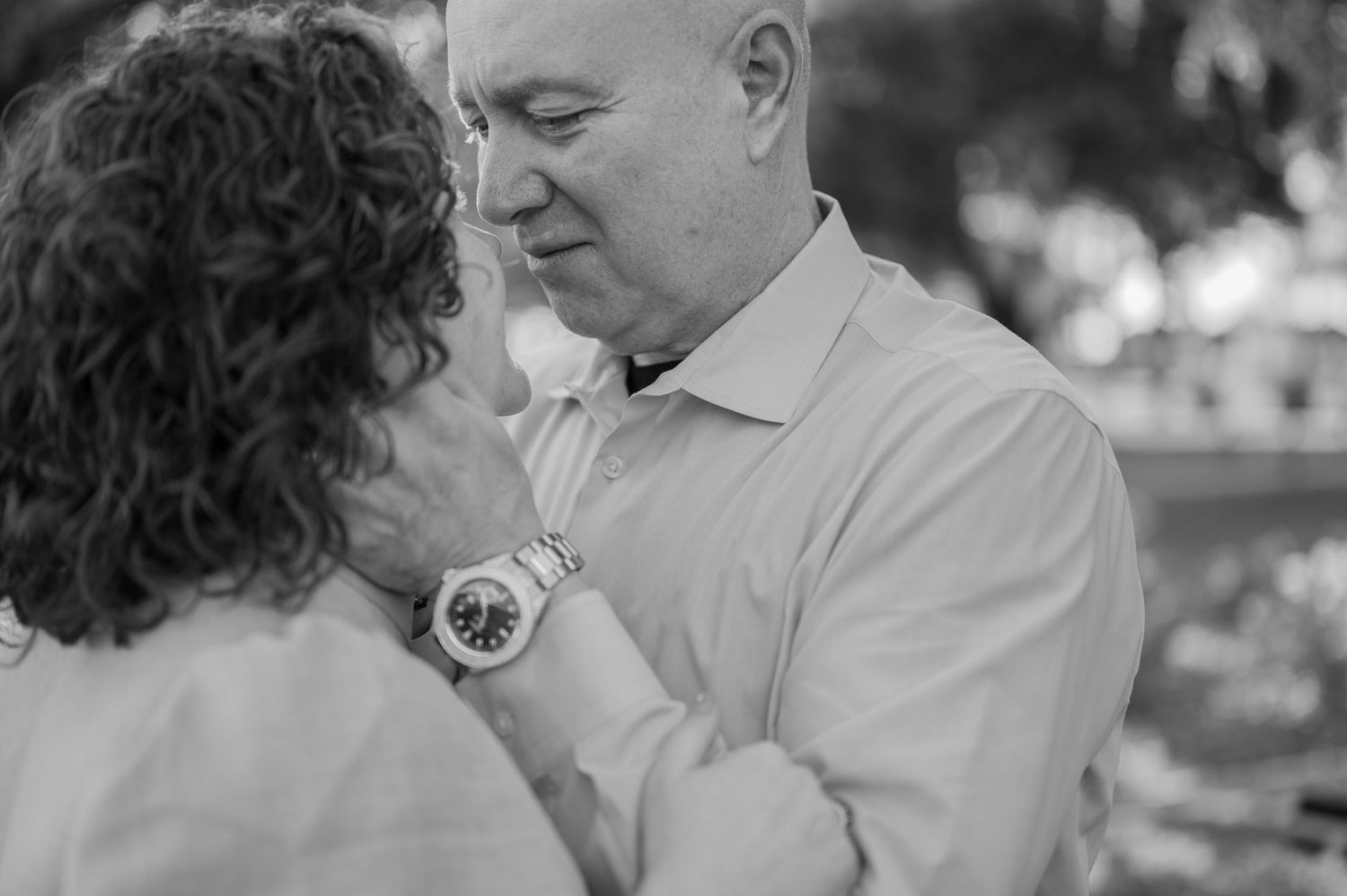 Black and white photo of a couple sharing an intimate moment, man wearing a watch gently holds woman's face.