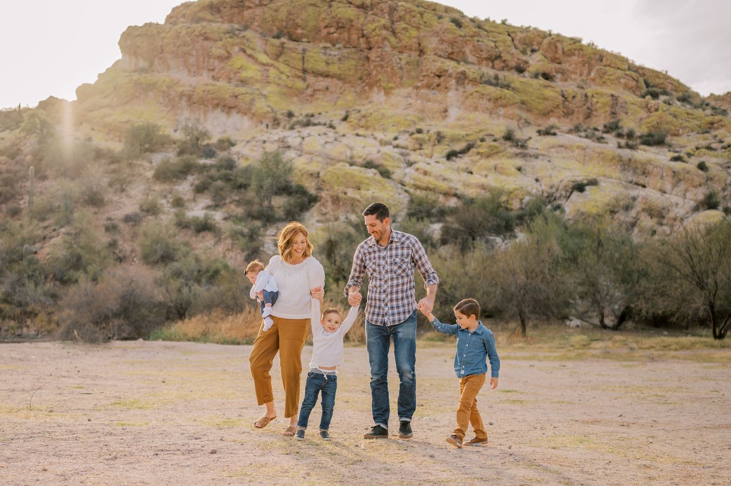 Family walking together through a desert landscape with mountains in the background. Phoenix Arizona family photographer.