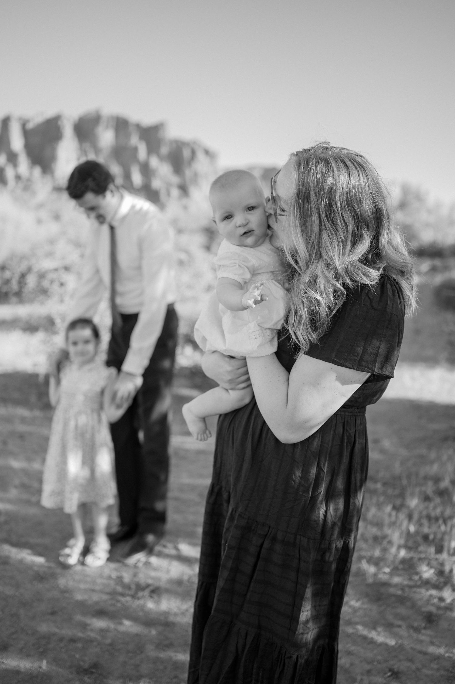 Black and white family photo of a mother kissing her baby outdoors. Arizona family photographer