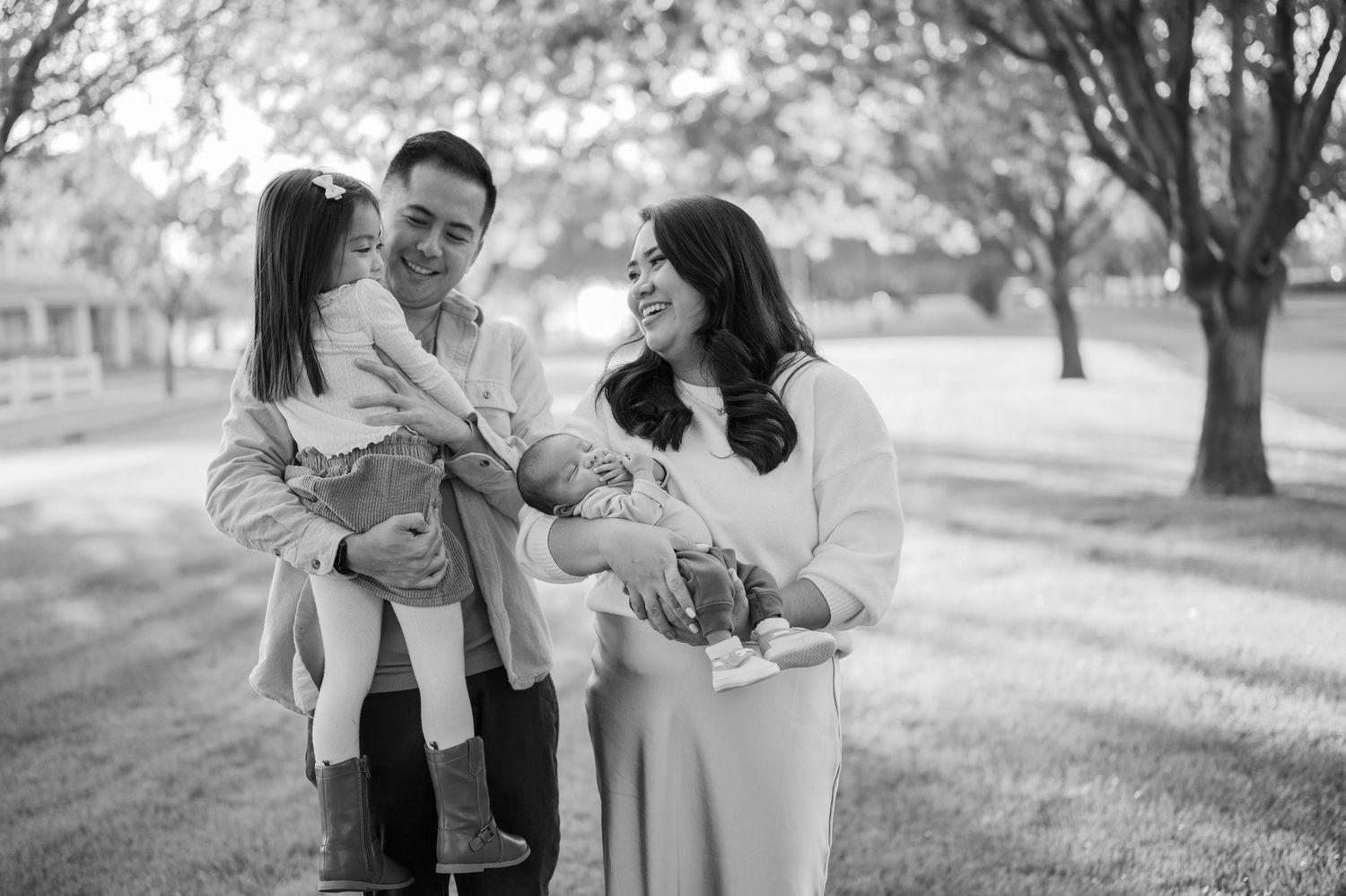 A series of black and white photos showing tender family moments in a park setting with parents and children playing together.