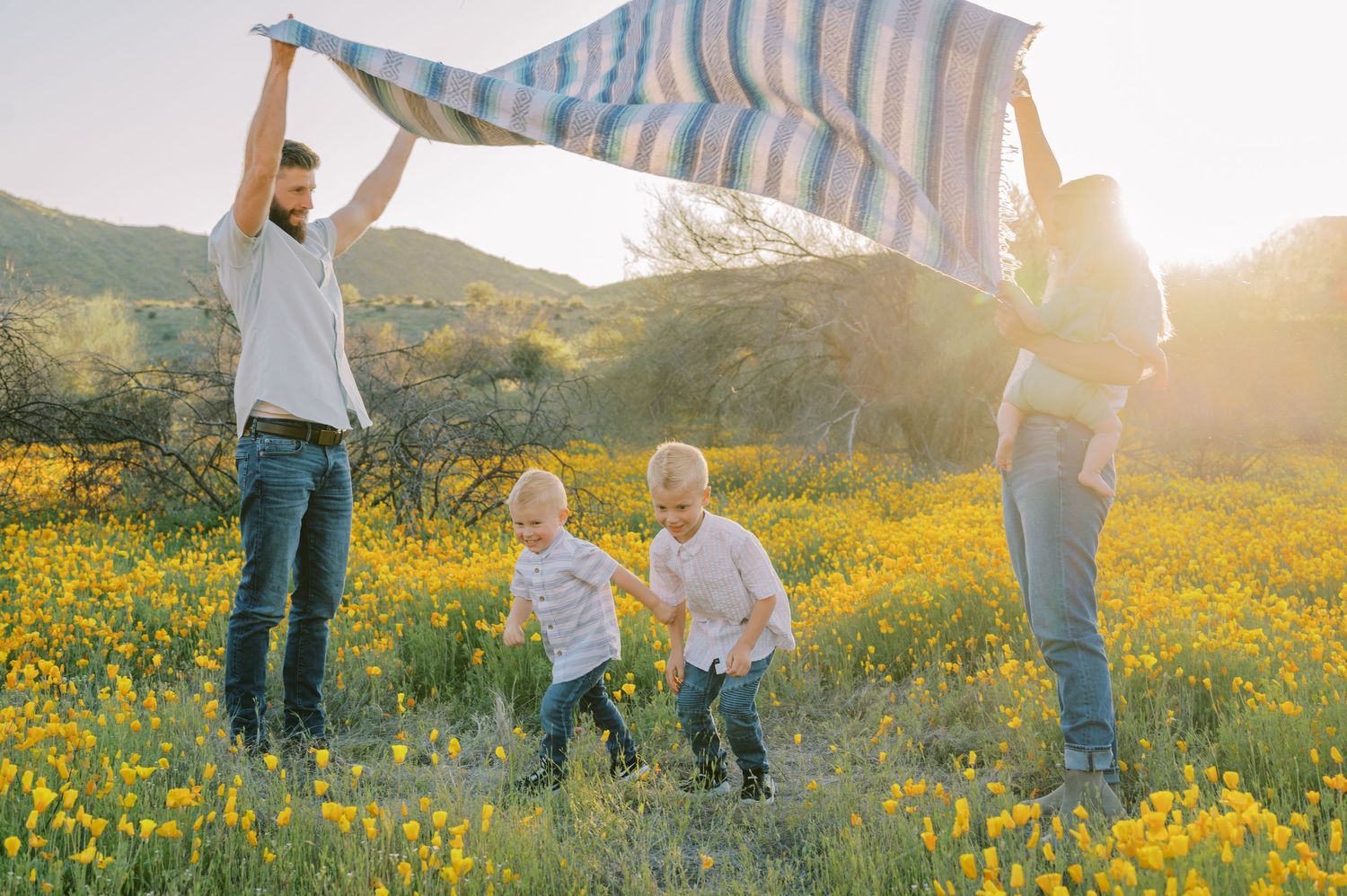 Family walking through a sunlit meadow of yellow wildflowers at sunset with mountains in the background. Phoenix Arizona family photographer