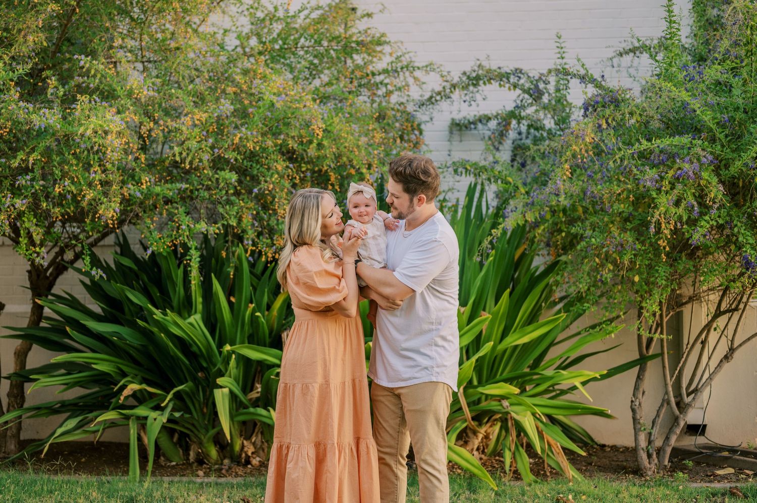 A couple shares a tender moment in a lush garden setting with tropical plants and greenery. Phoenix Arizona family photographer.
