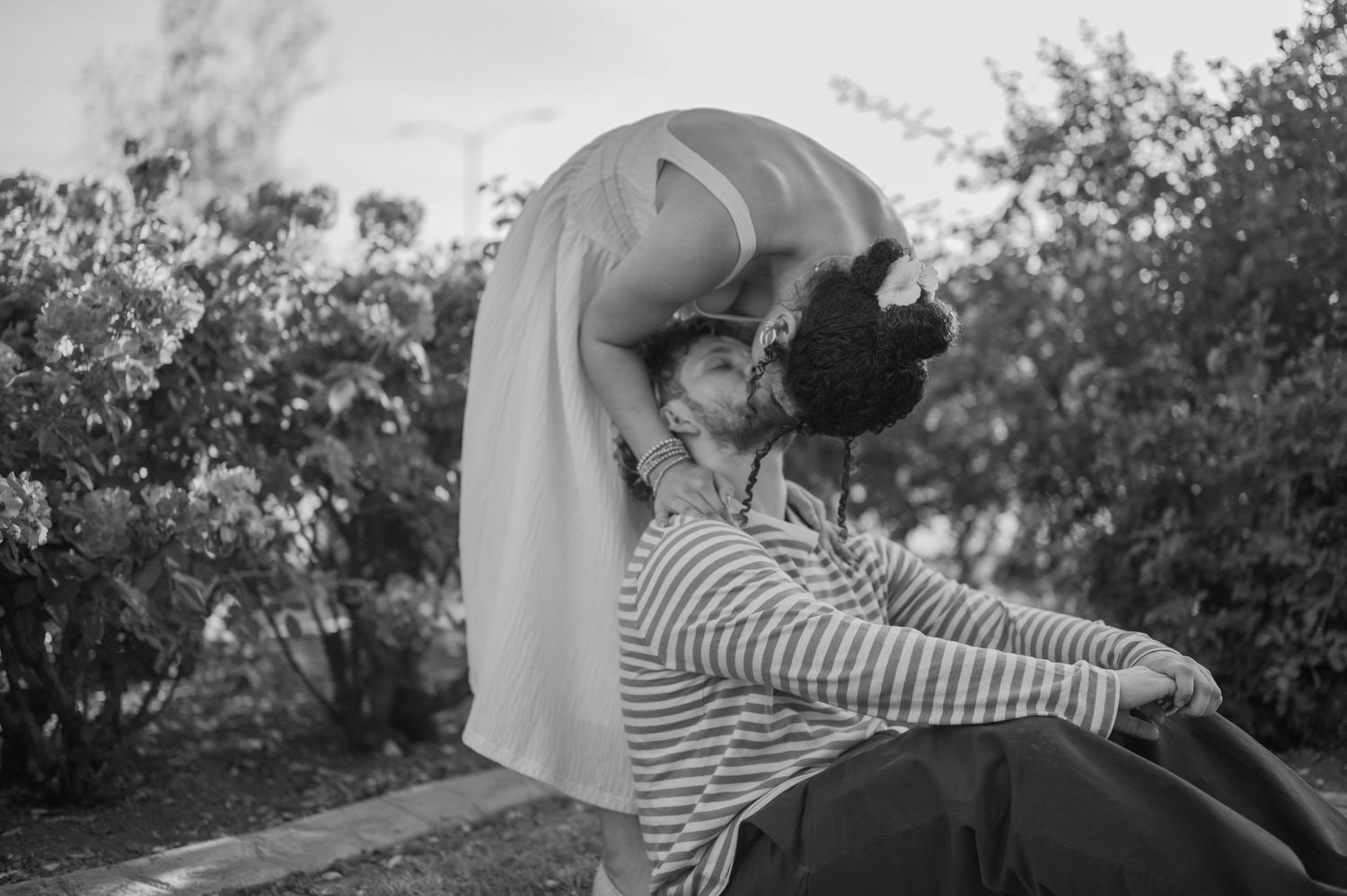 Black and white photo of a couple sharing a romantic kiss outdoors, surrounded by lush greenery.
