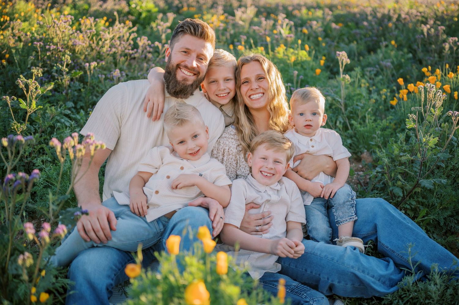 Family sitting together outdoors in a garden with yellow wildflowers during golden hour sunset. Phoenix Arizona family photographer.