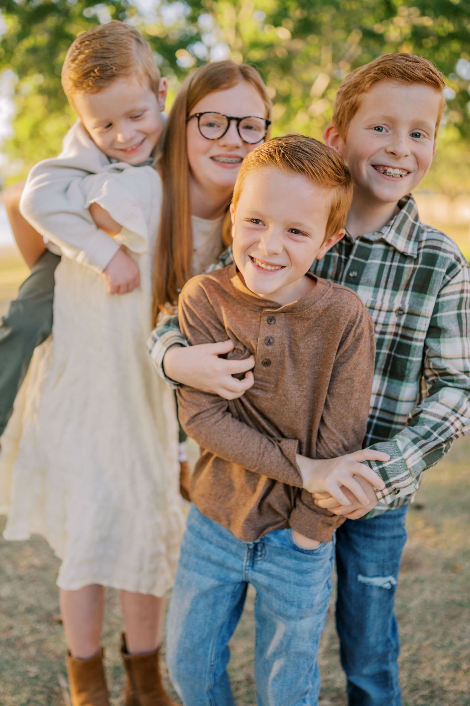 Four siblings share a joyful moment together outdoors in warm sunlight wearing casual clothing. Phoenix Arizona family photographer.
