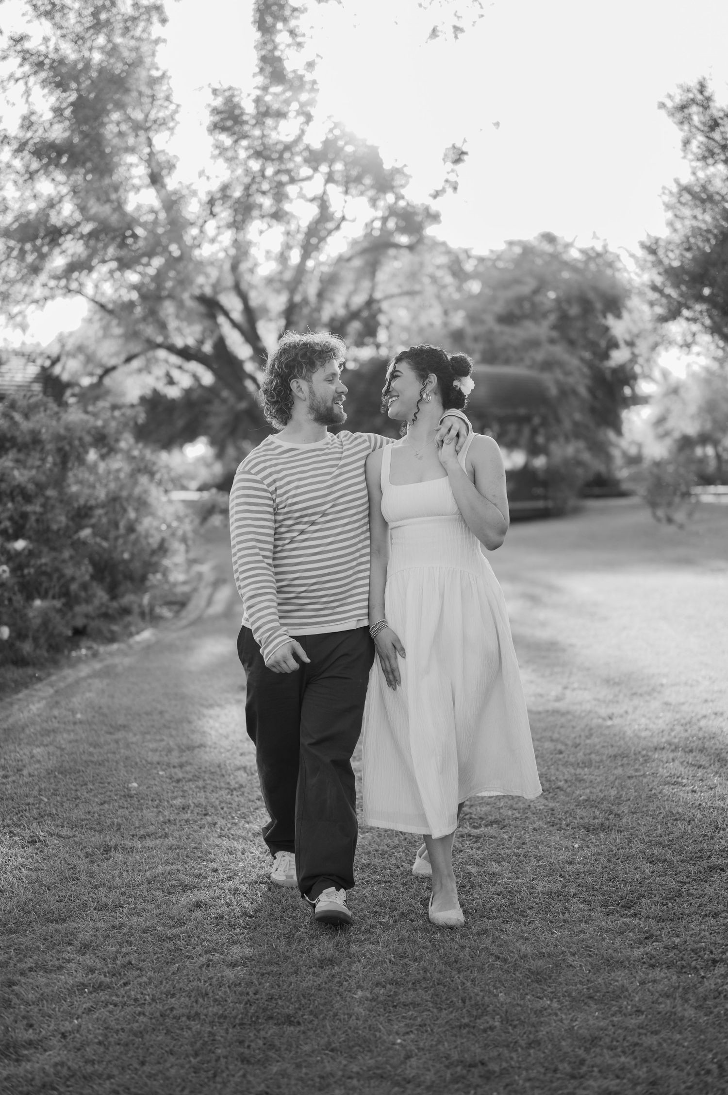 Black and white photo of a couple walking and gazing at each other in a lush garden path.
