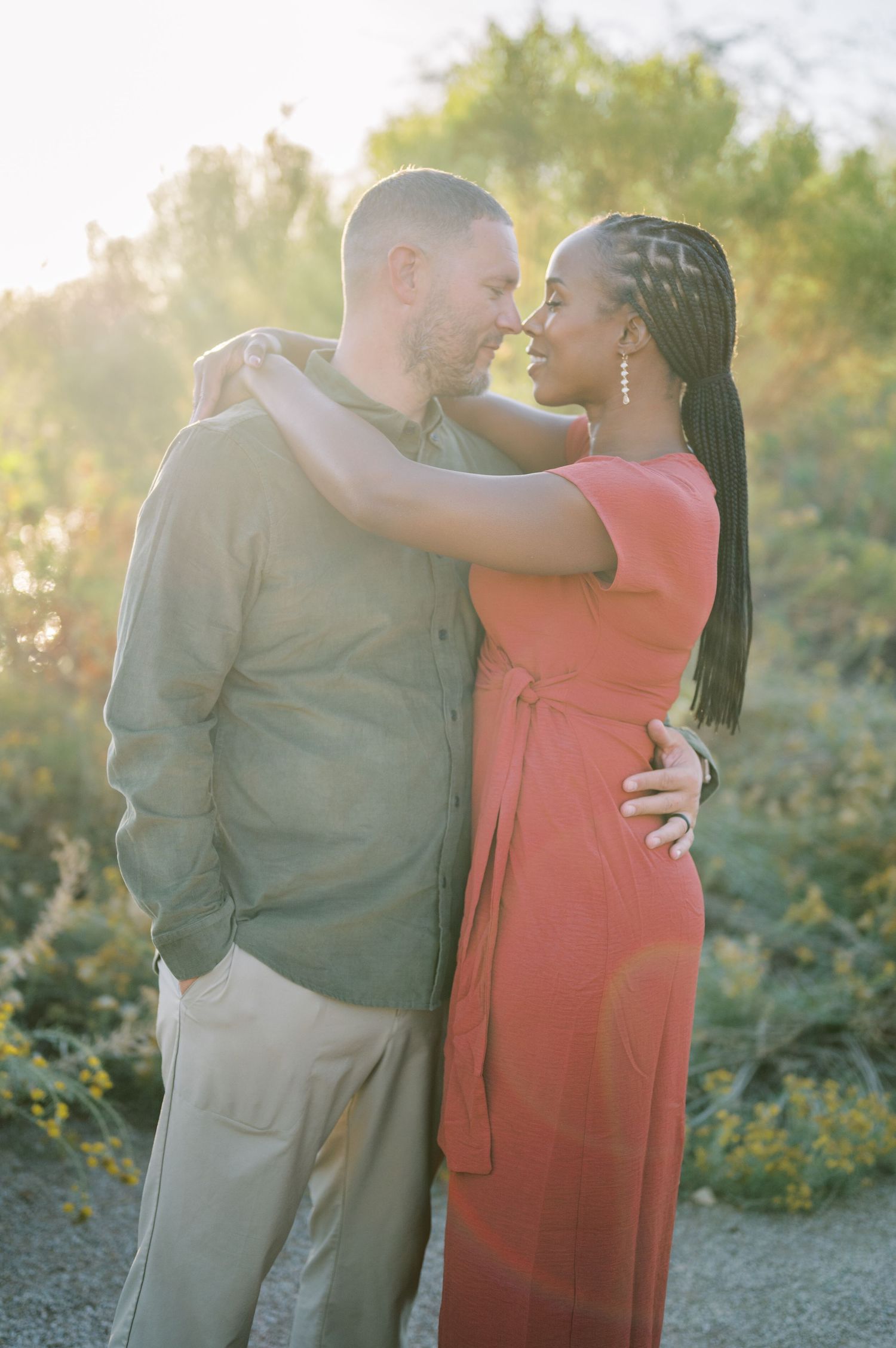 A couple in a romantic embrace outdoors during golden hour with a coral dress and olive suit. Phoenix Arizona couples photographer.