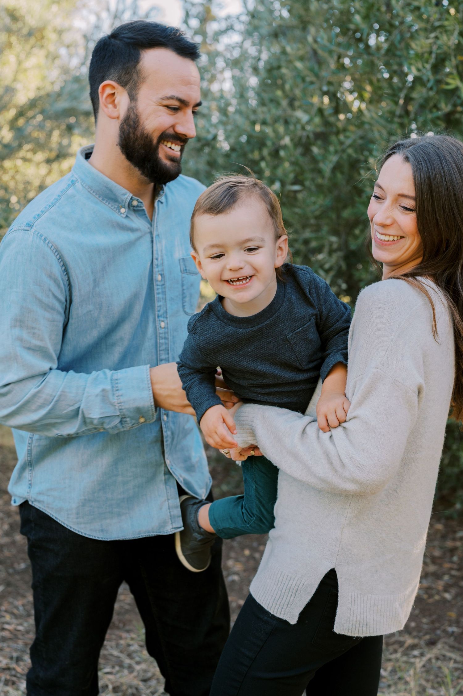A joyful family shares candid moments of laughter and embraces while wearing casual sweaters outdoors. Phoenix Arizona family photographer.