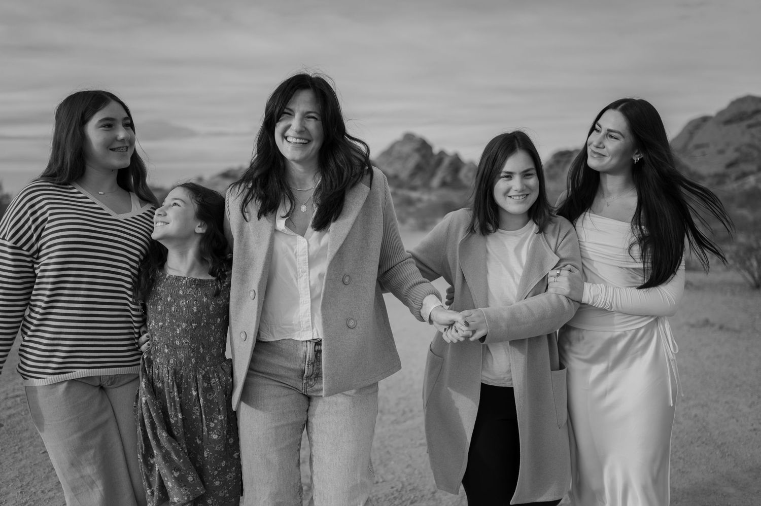 Black and white photo of a group walking and laughing together with mountains in the background. Phoenix Arizona family photographer.