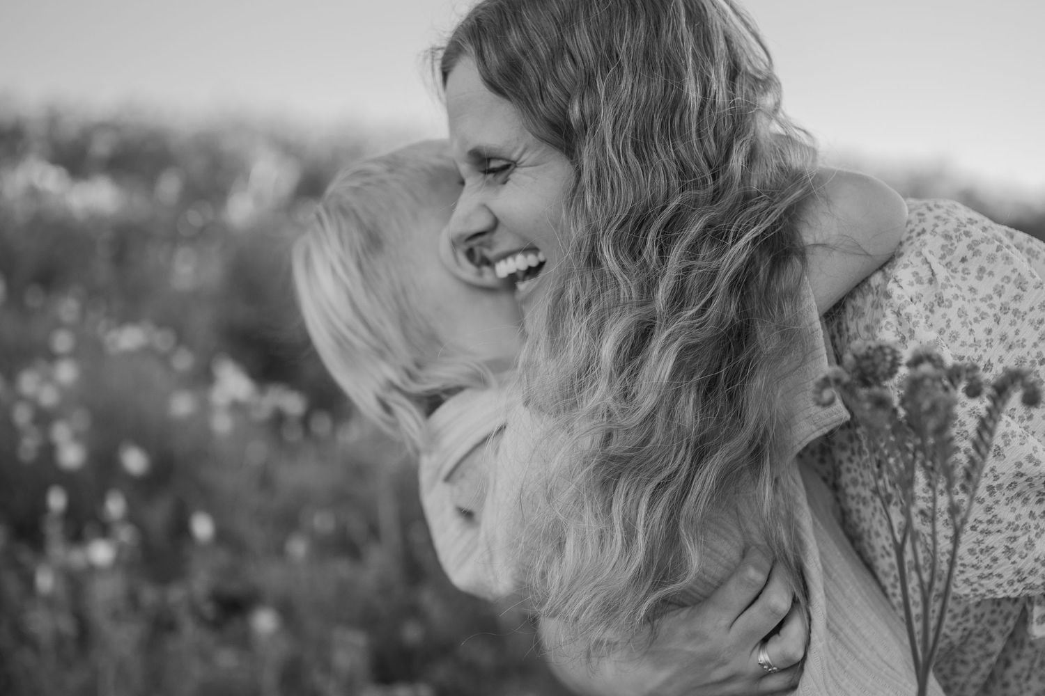 Black and white portrait of joyful moment between two people with wavy hair in a field of flowers. Phoenix Arizona family photographer.